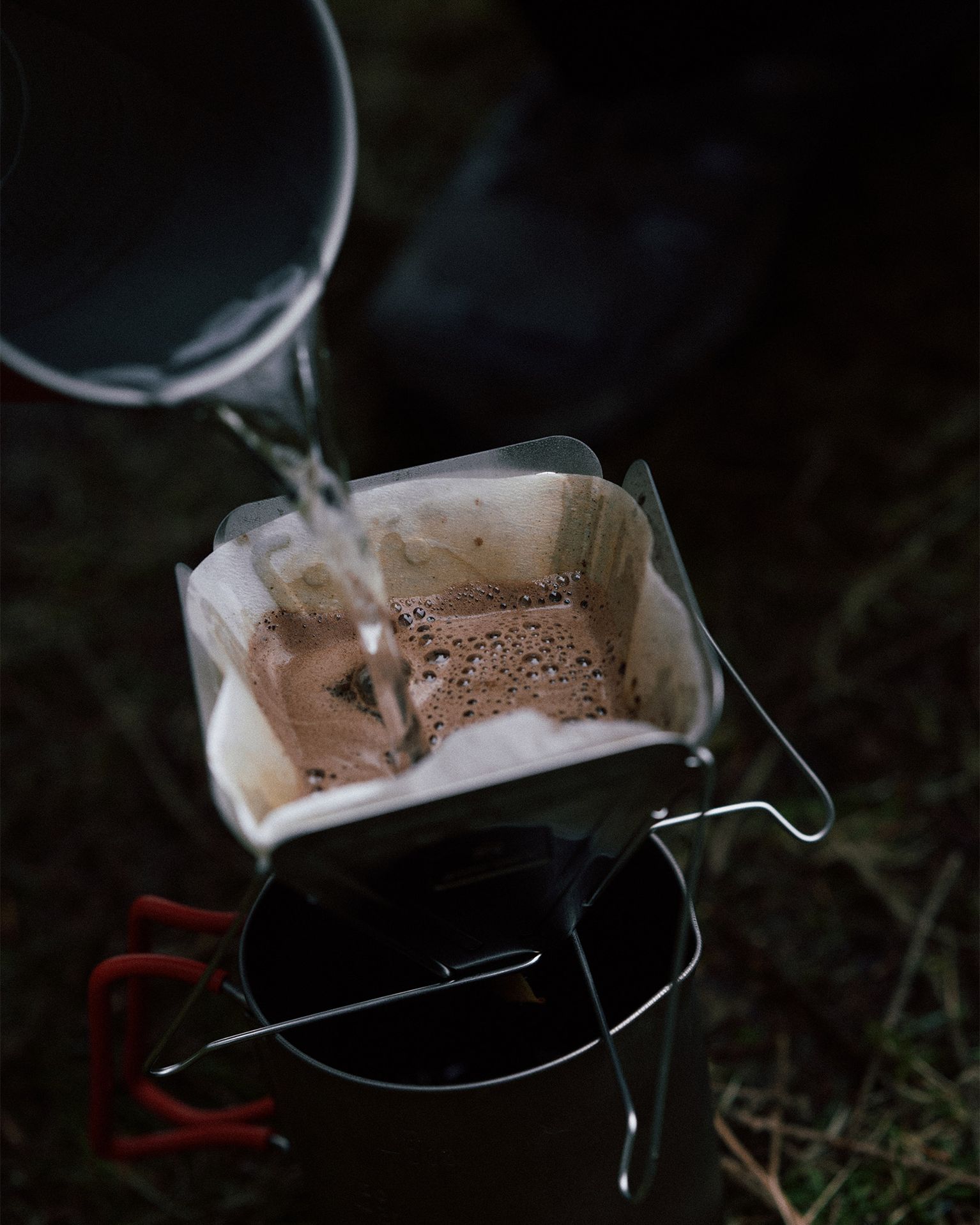 Pouring hot water over coffee grounds in a filter atop a camping mug, outdoors.