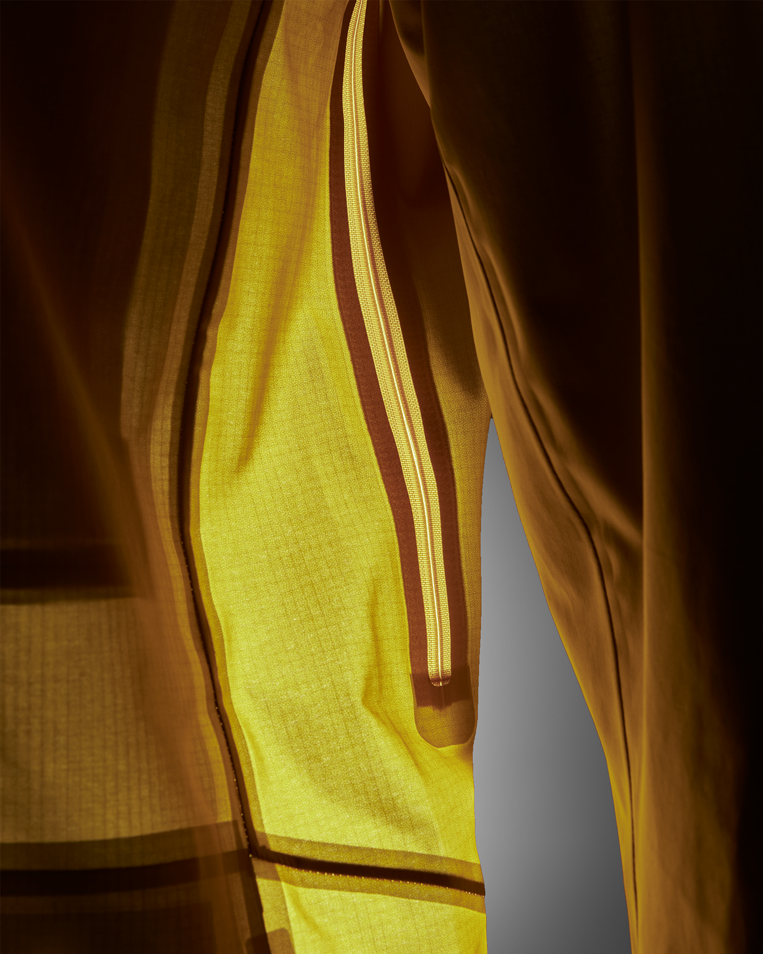Close-up of a yellow jacket with a zipper and dark brown stripes, illuminated to highlight the fabric texture and design details.