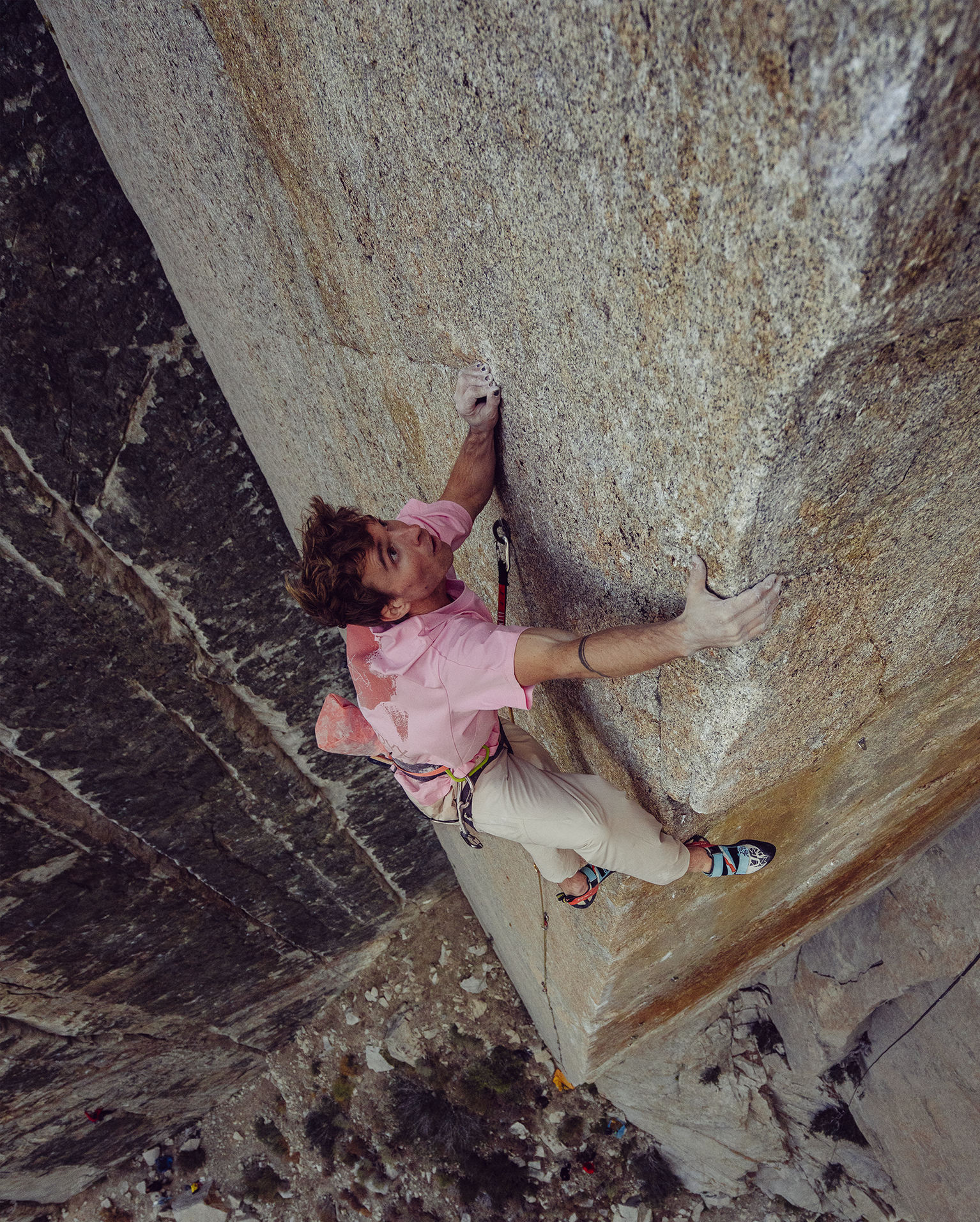 Climber grips vertical rock face, wearing a pink Arc'teryx shirt and climbing gear, showcasing strength and focus high above the ground.