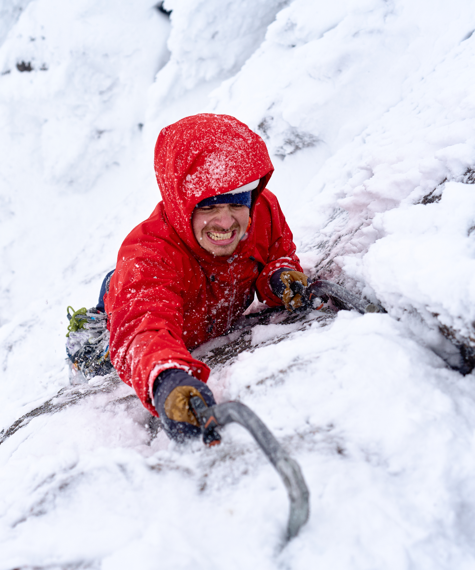 Climber in a red jacket scaling a snowy mountain face, gripping an ice axe with determination.