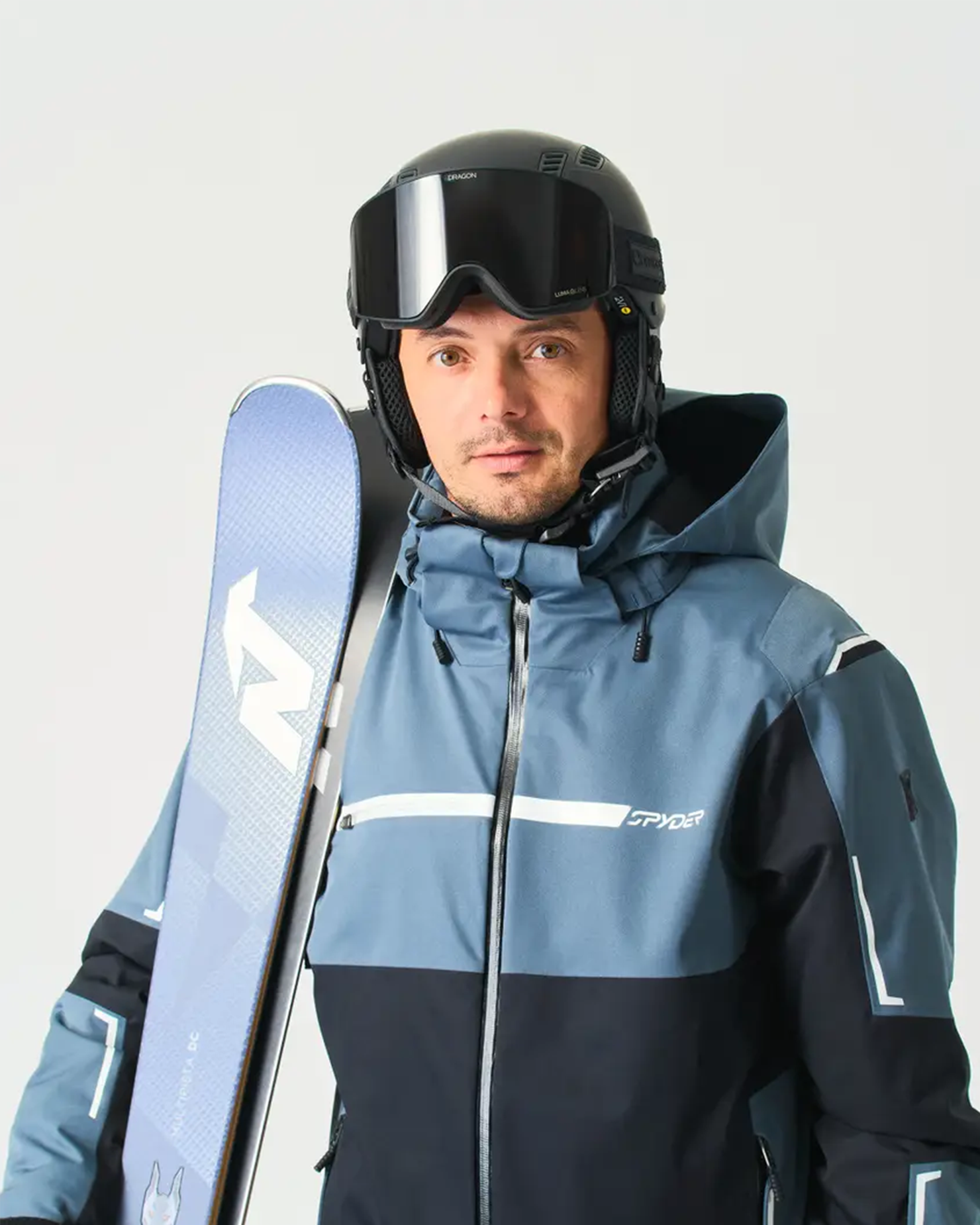 skier in blue and black jacket, helmet and goggles holding a blue ski