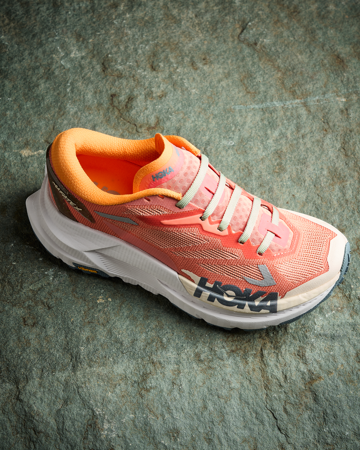 Orange and pink trail running shoe with a thick white sole, set on a textured stone surface.
