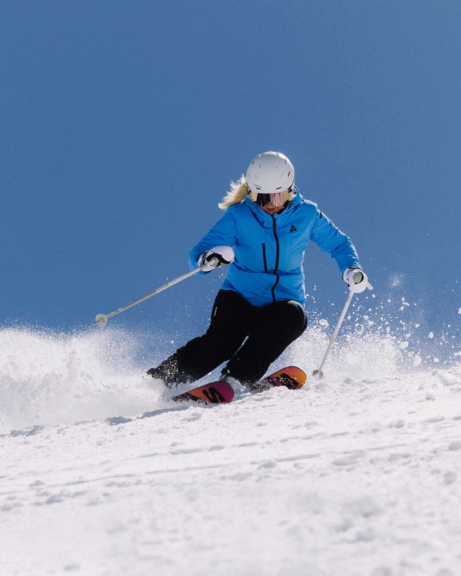A skier in a blue jacket and helmet expertly descends a snowy slope under a clear blue sky.