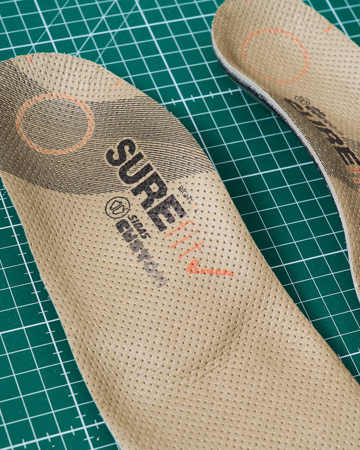 Two beige insoles with text markings, placed on a green grid cutting mat.