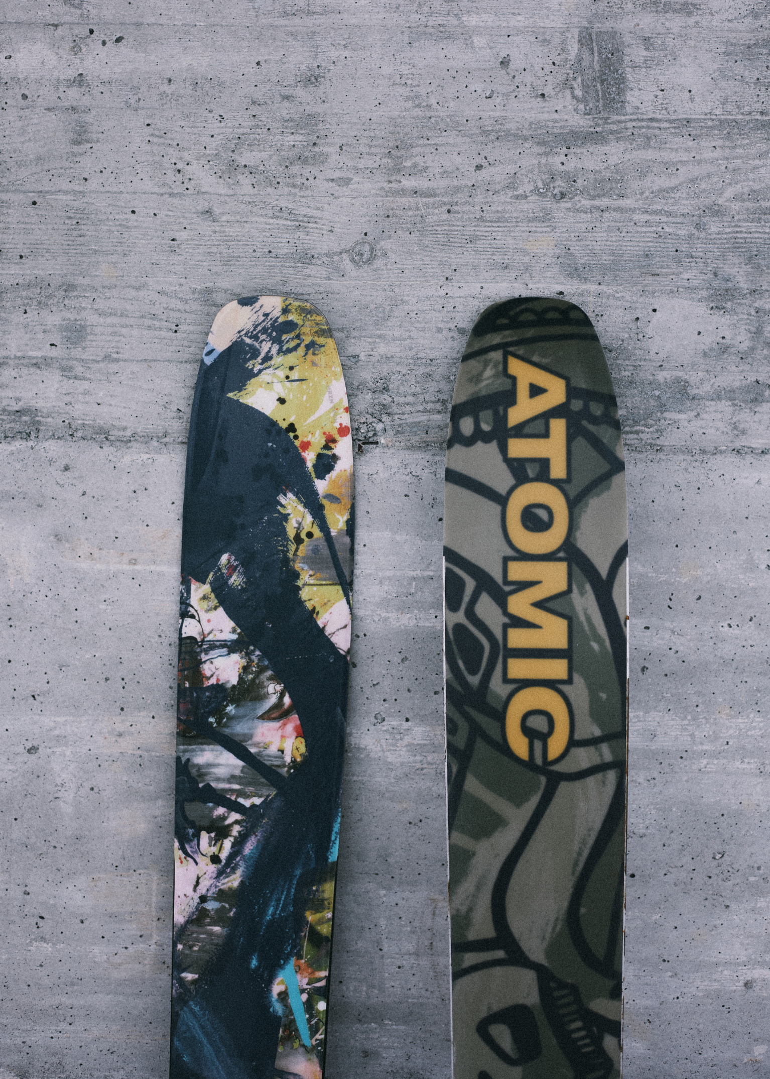 Close-up of two skis with colourful abstract designs resting on a textured concrete surface.