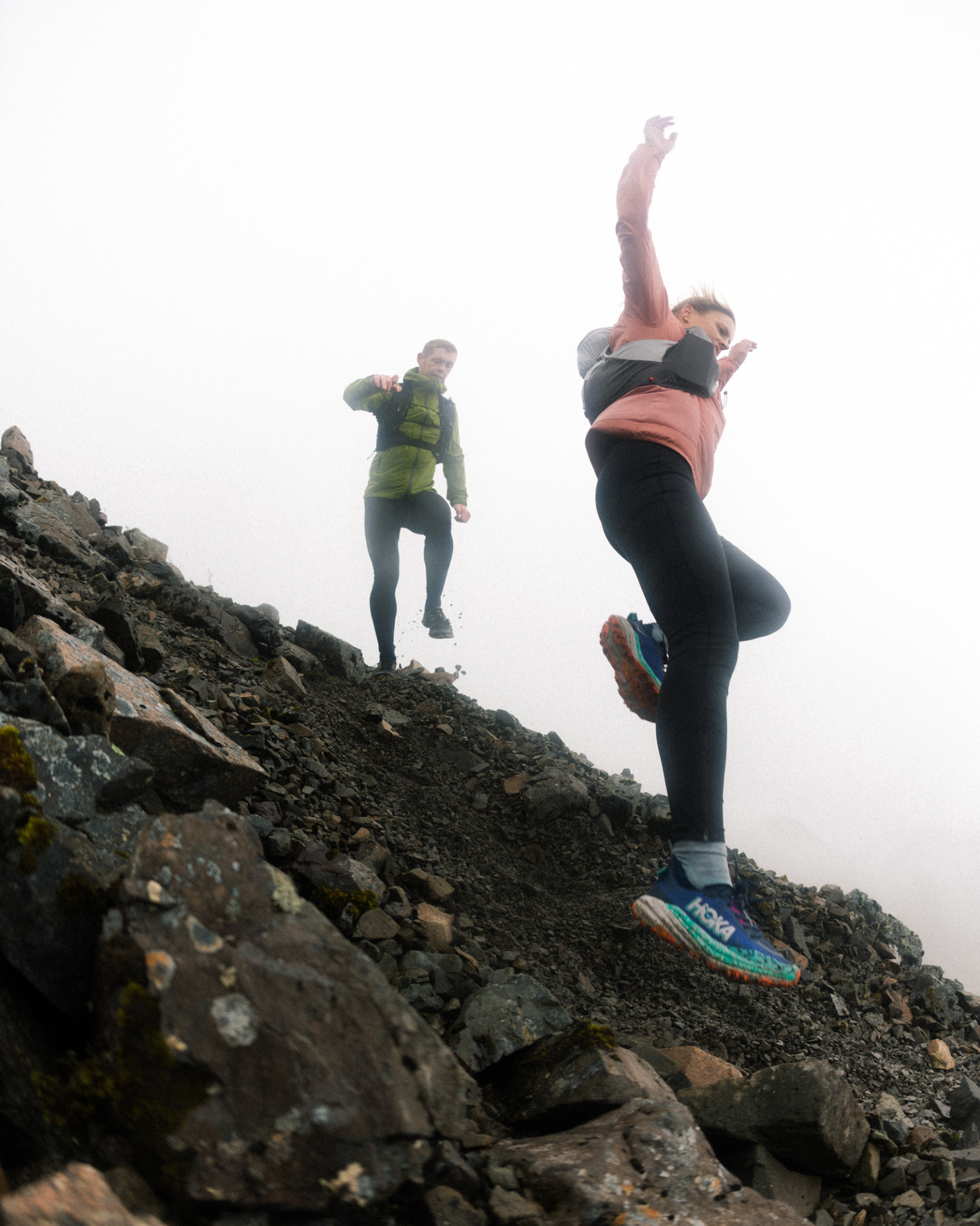 Two people trail running down a rocky, foggy mountain slope, showcasing dynamic movement and outdoor adventure.