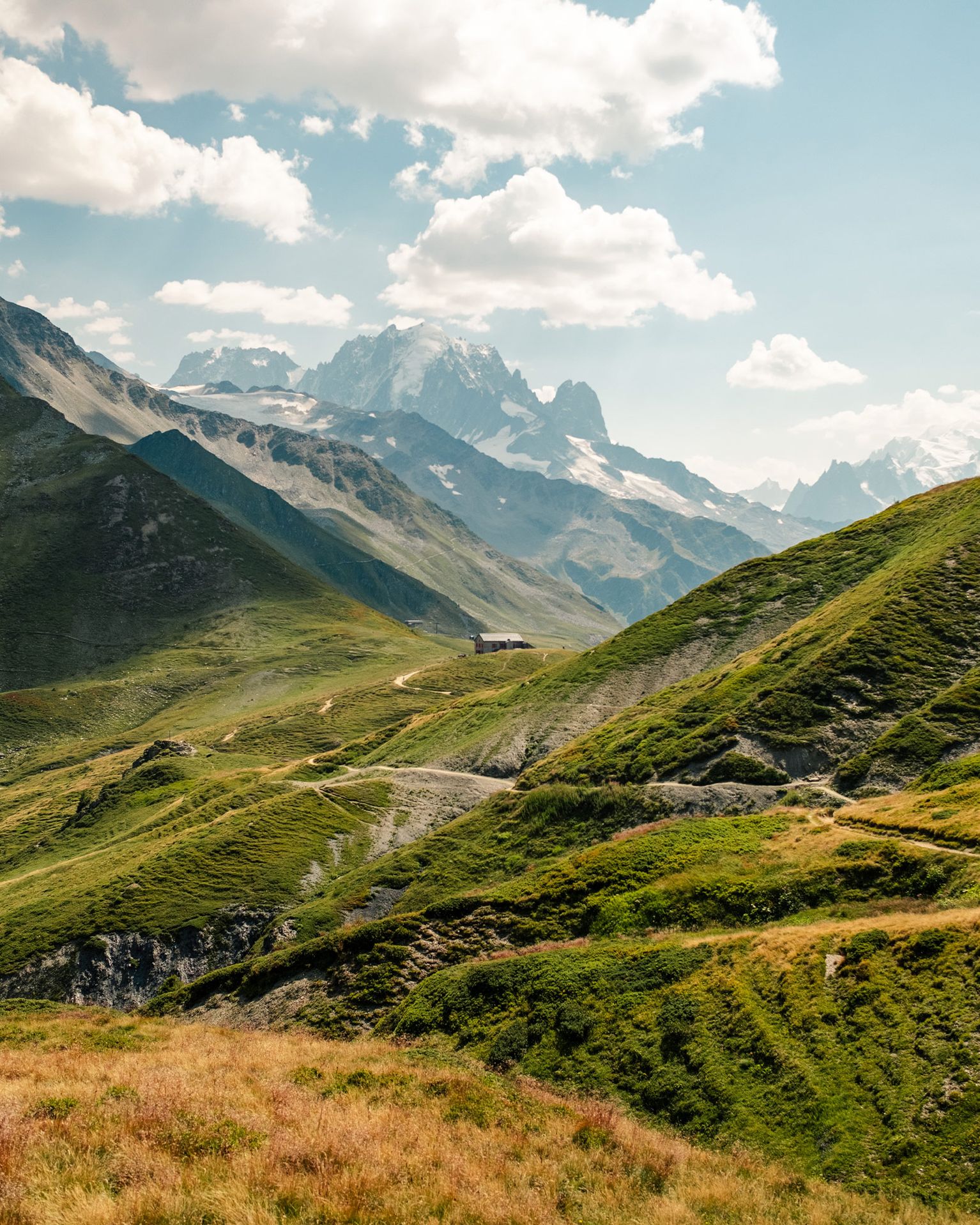 Scenic view of lush green rolling hills and mountains under a cloudy sky, with a distant snow-capped peak.