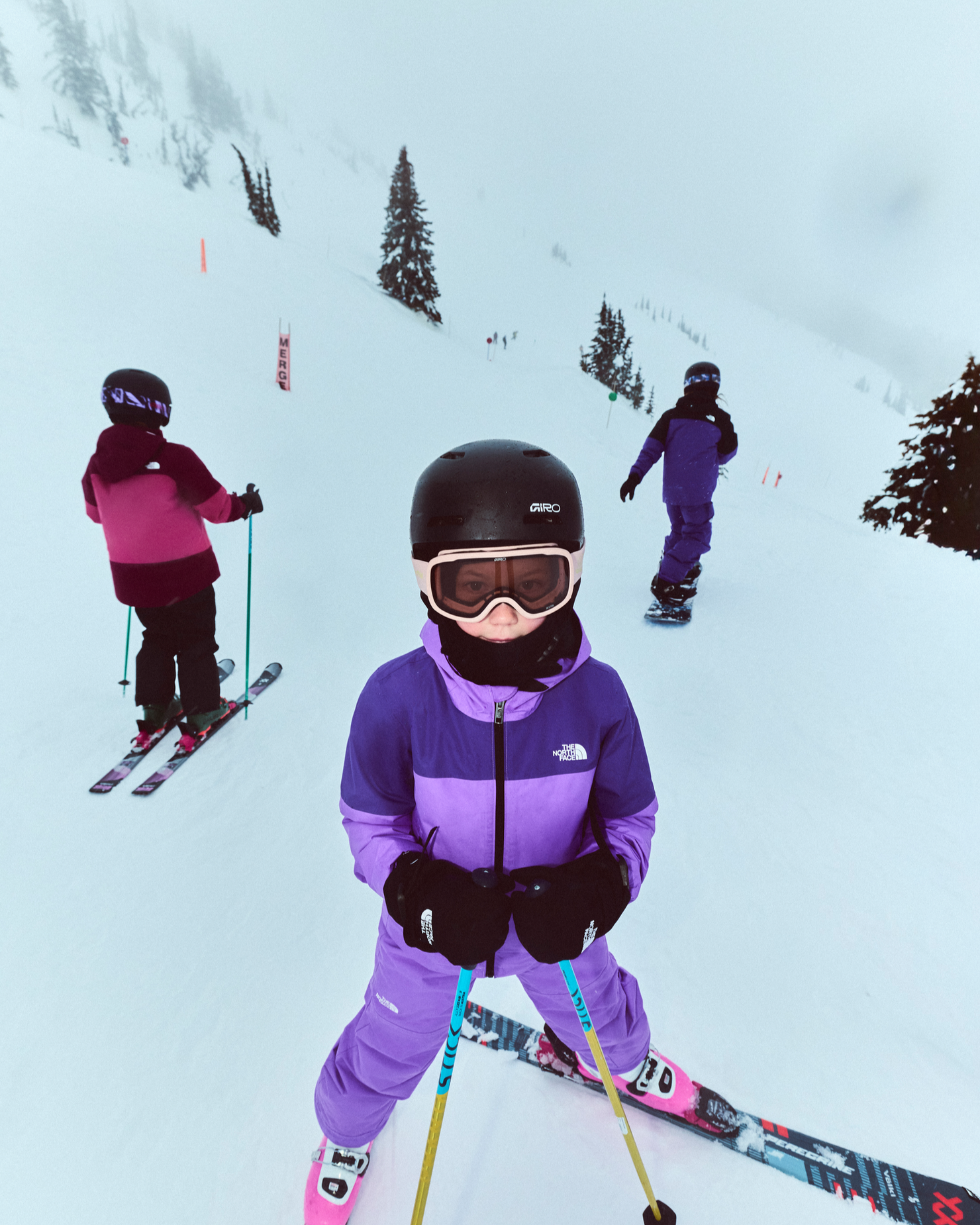 Children skiing and snowboarding on a snowy mountain, dressed in high-quality gear.