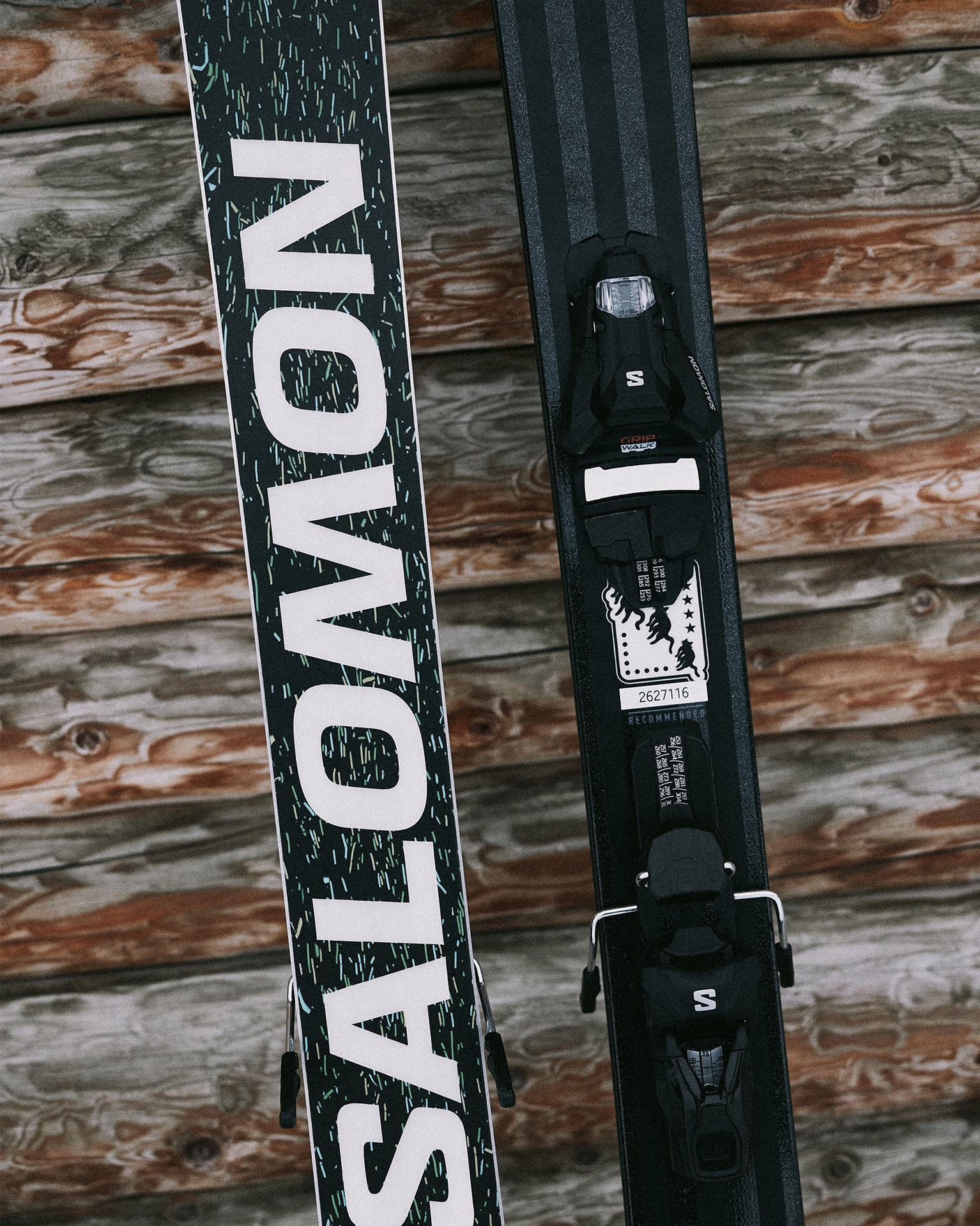 Close-up of Salomon skis with bindings leaning against a wooden wall.