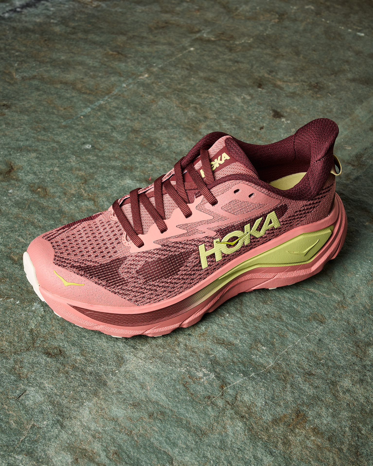 Pink and maroon trail running shoe with yellow accents, featuring a thick sole, on a stone surface.