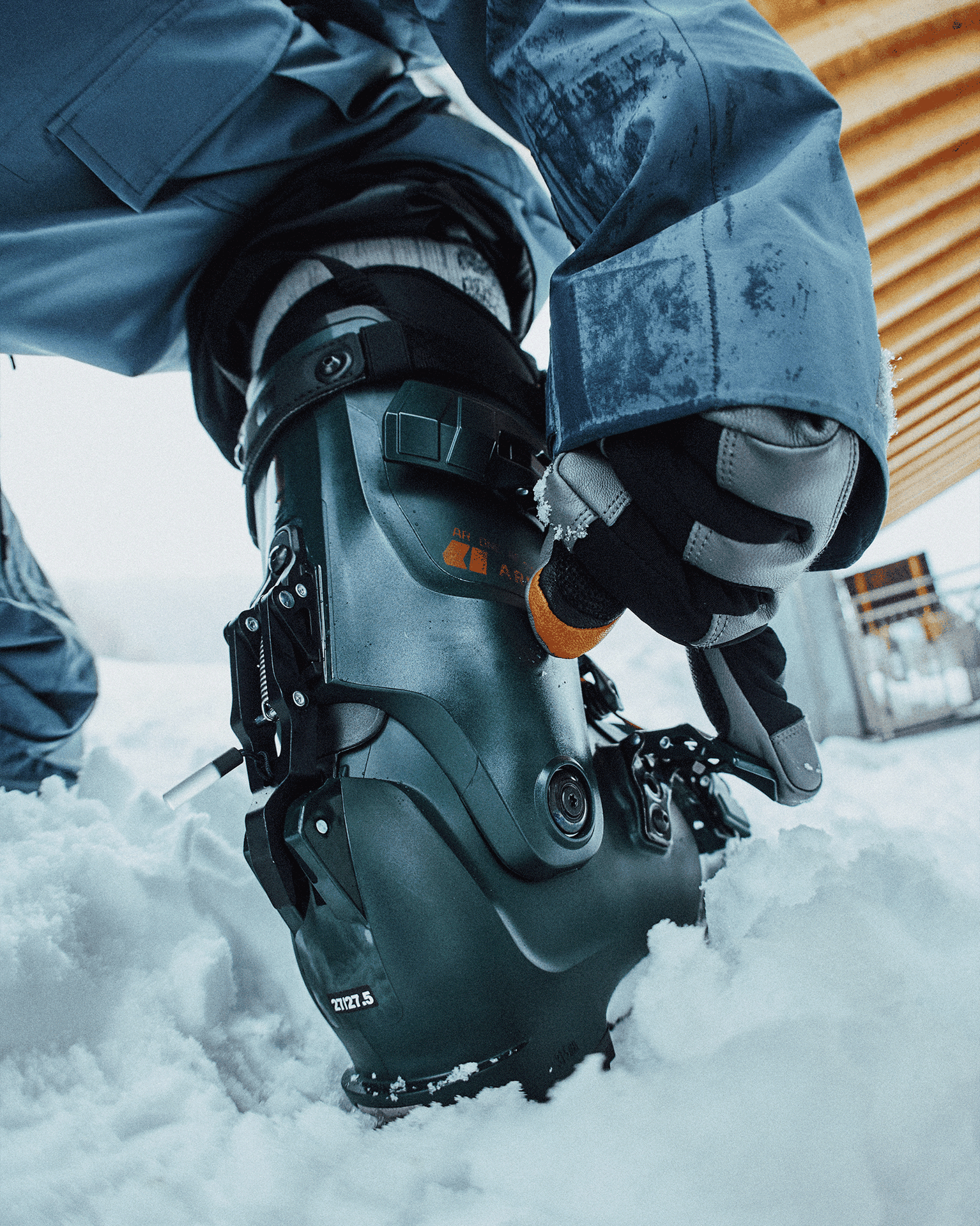 Person adjusting a black ski boot in a snowy environment.