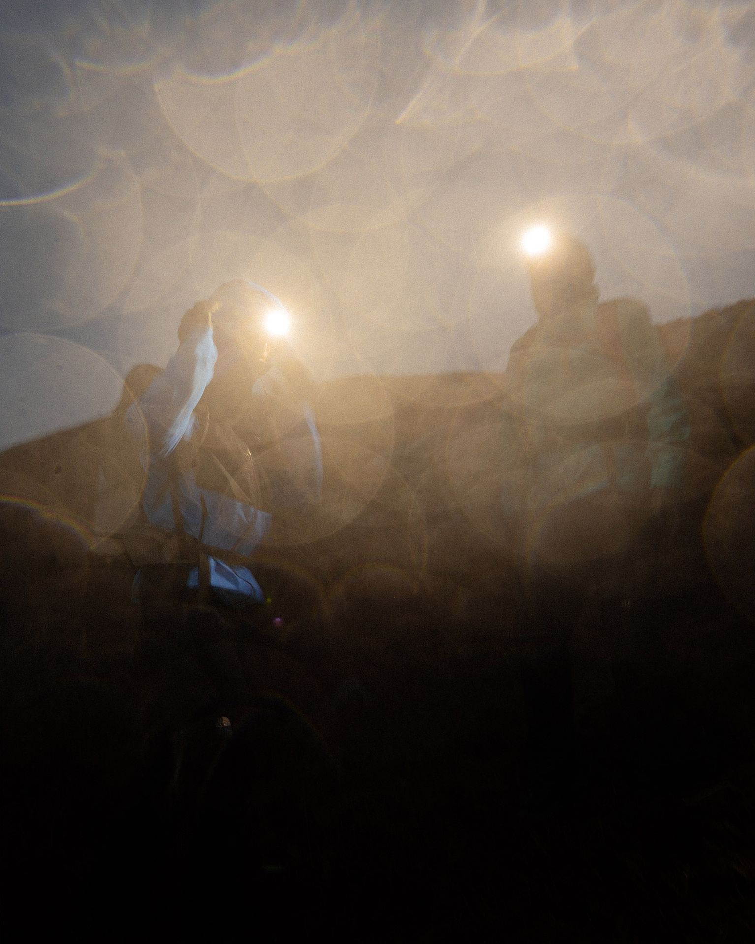 Two hikers with headlamps in a foggy, dimly lit setting, creating a dreamy, ethereal atmosphere with light reflections.