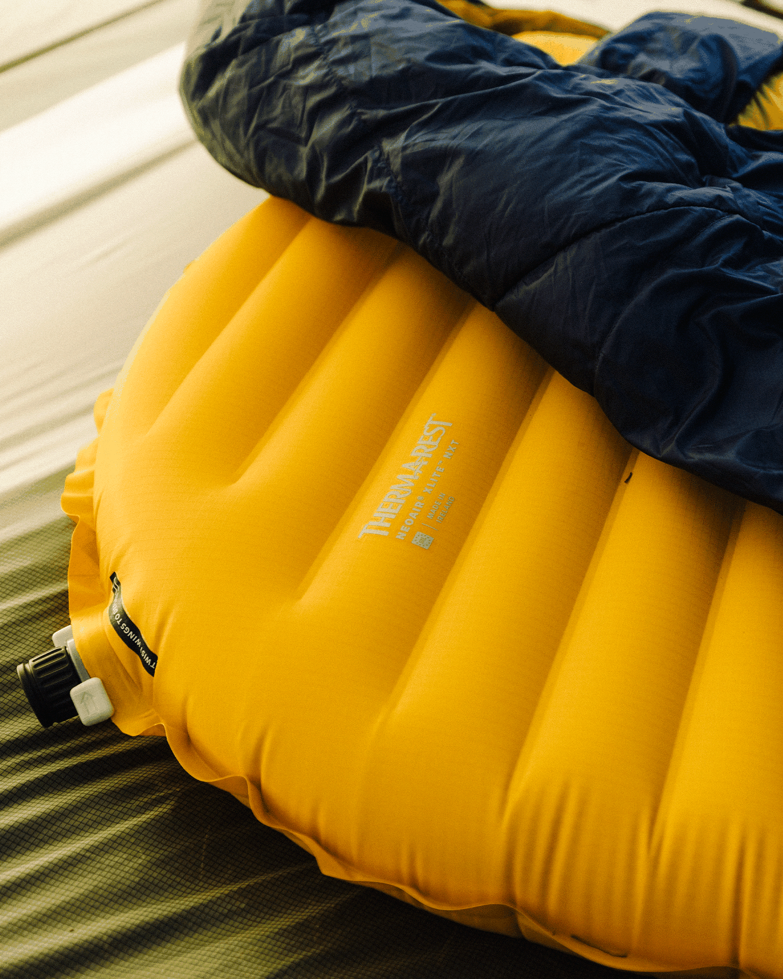 Yellow inflatable sleeping mat with a navy sleeping bag on top, designed for mountain sports comfort and easy set-up.