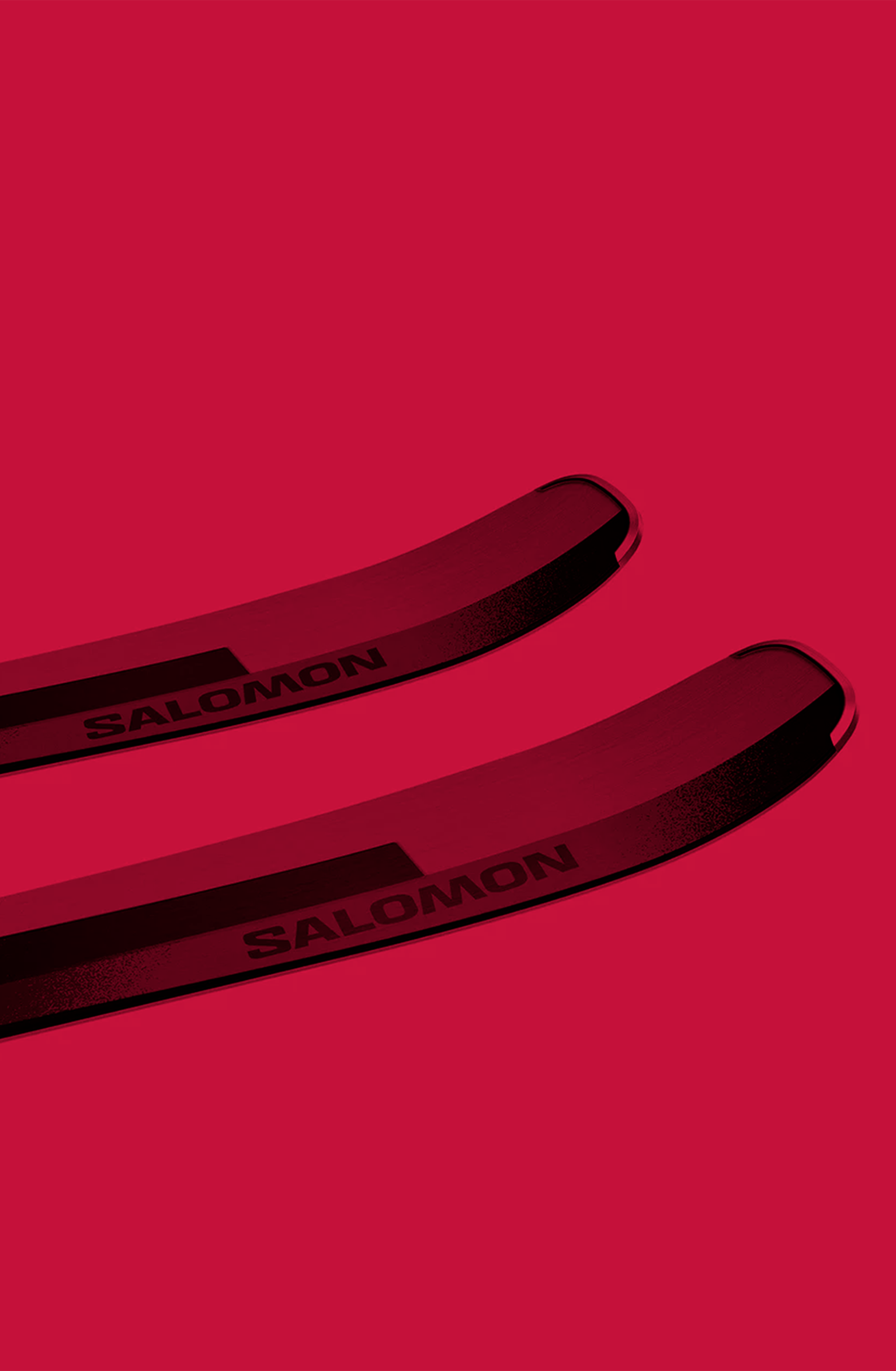 Close-up of two black and red Salomon skis on a vibrant red background, showing the brand name prominently.