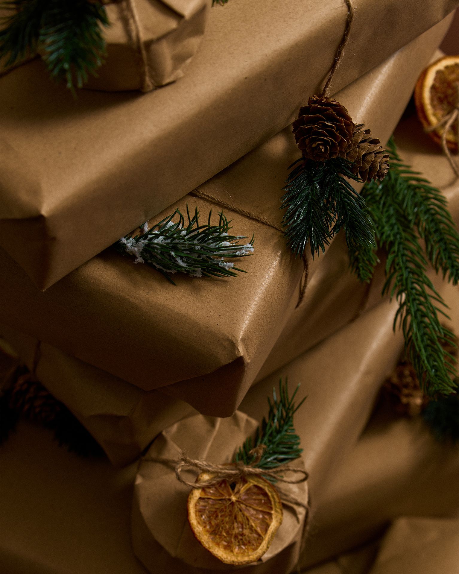Stacked brown paper parcels adorned with pine sprigs, pinecones, and dried orange slices, tied with twine.