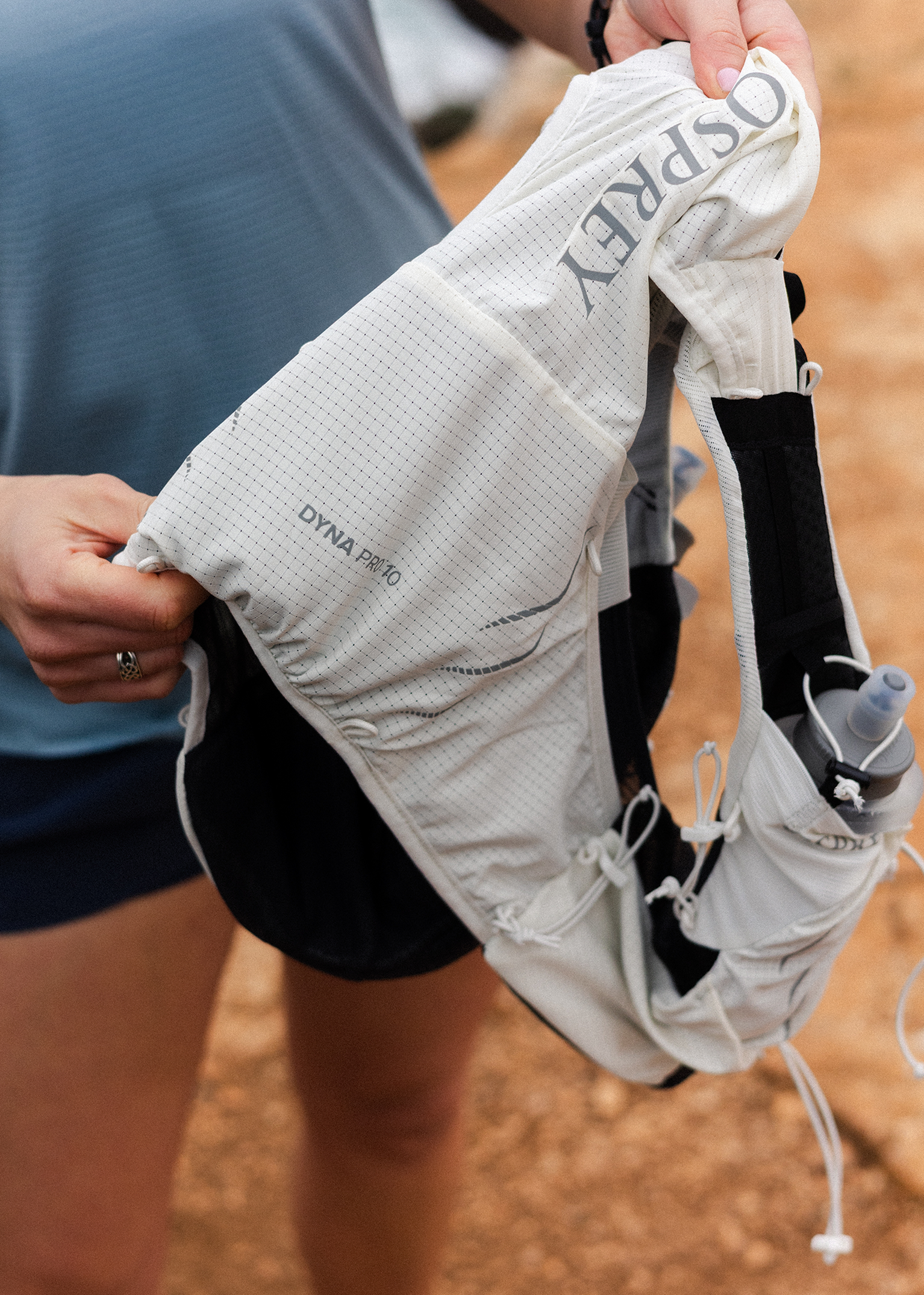 A person holding a white Osprey running vest with a small water bottle in the side pocket, detailed close-up.