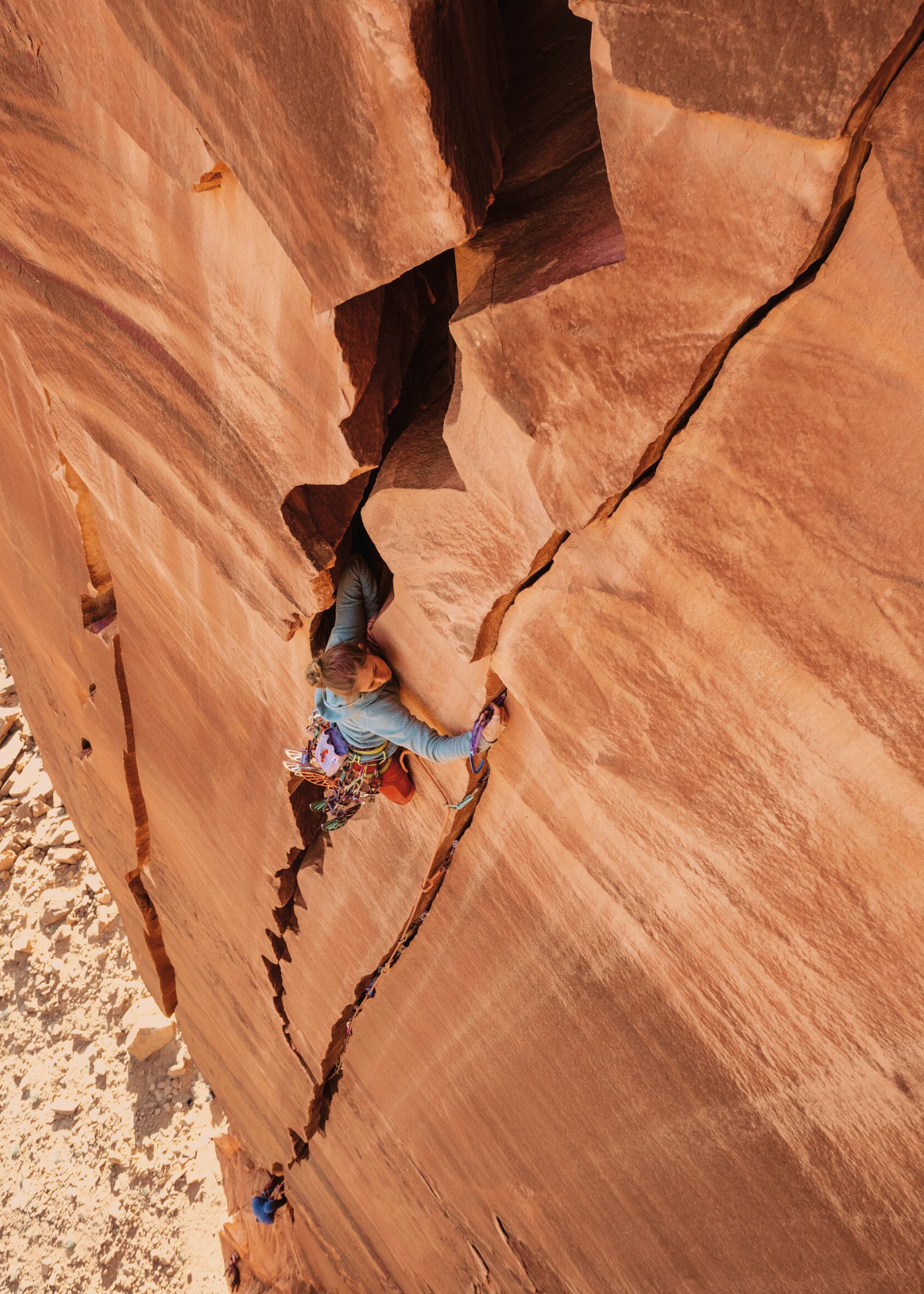 Climber ascending a steep, rugged rock face, gripping a narrow crack, showcasing skill and determination in a challenging mountain environment.