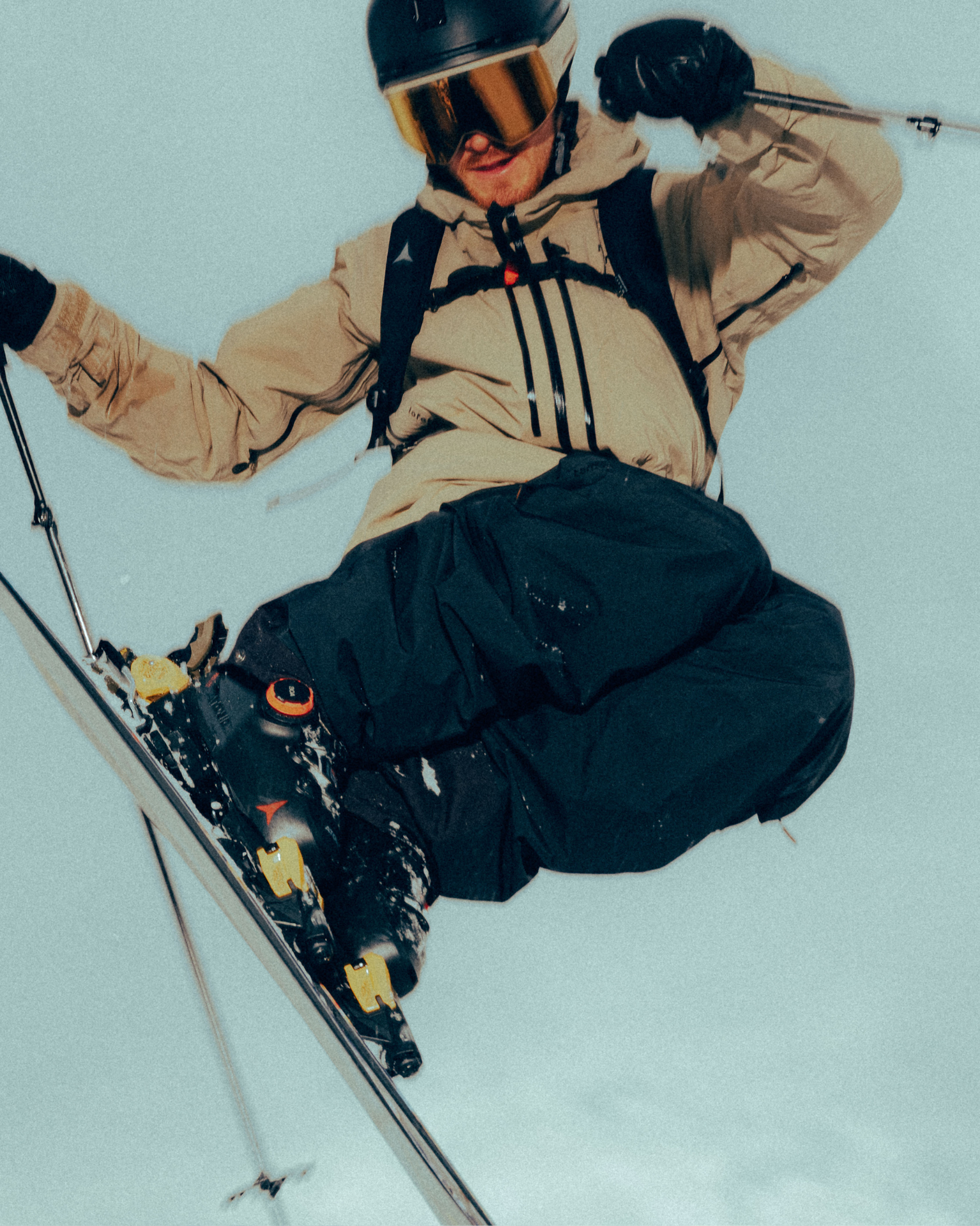 Skier executing an impressive jump, wearing a helmet, goggles, and winter gear, with poles in hand against a clear sky.