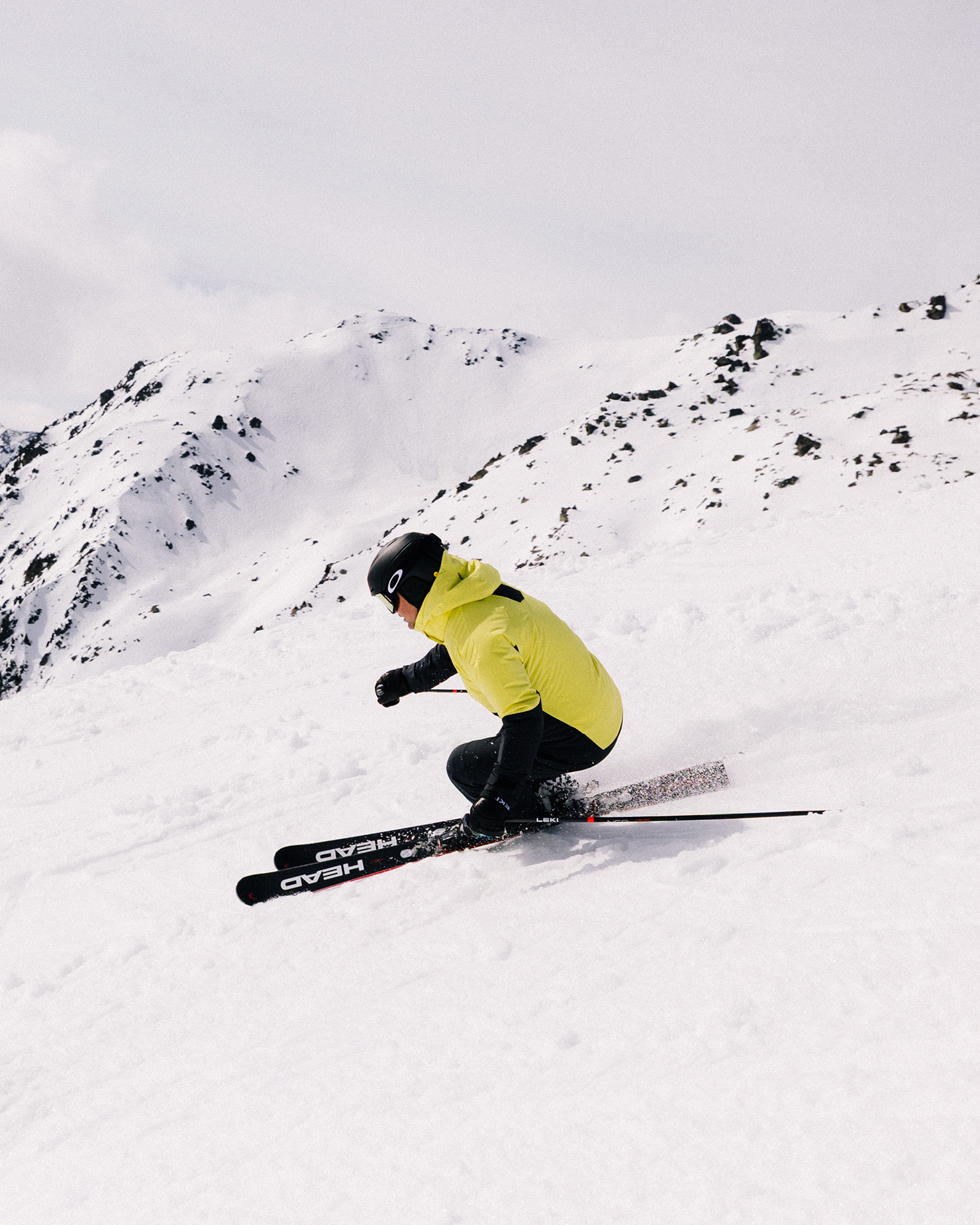 Skier in a bright yellow jacket expertly navigating a snowy mountain slope, with rugged peaks in the background.