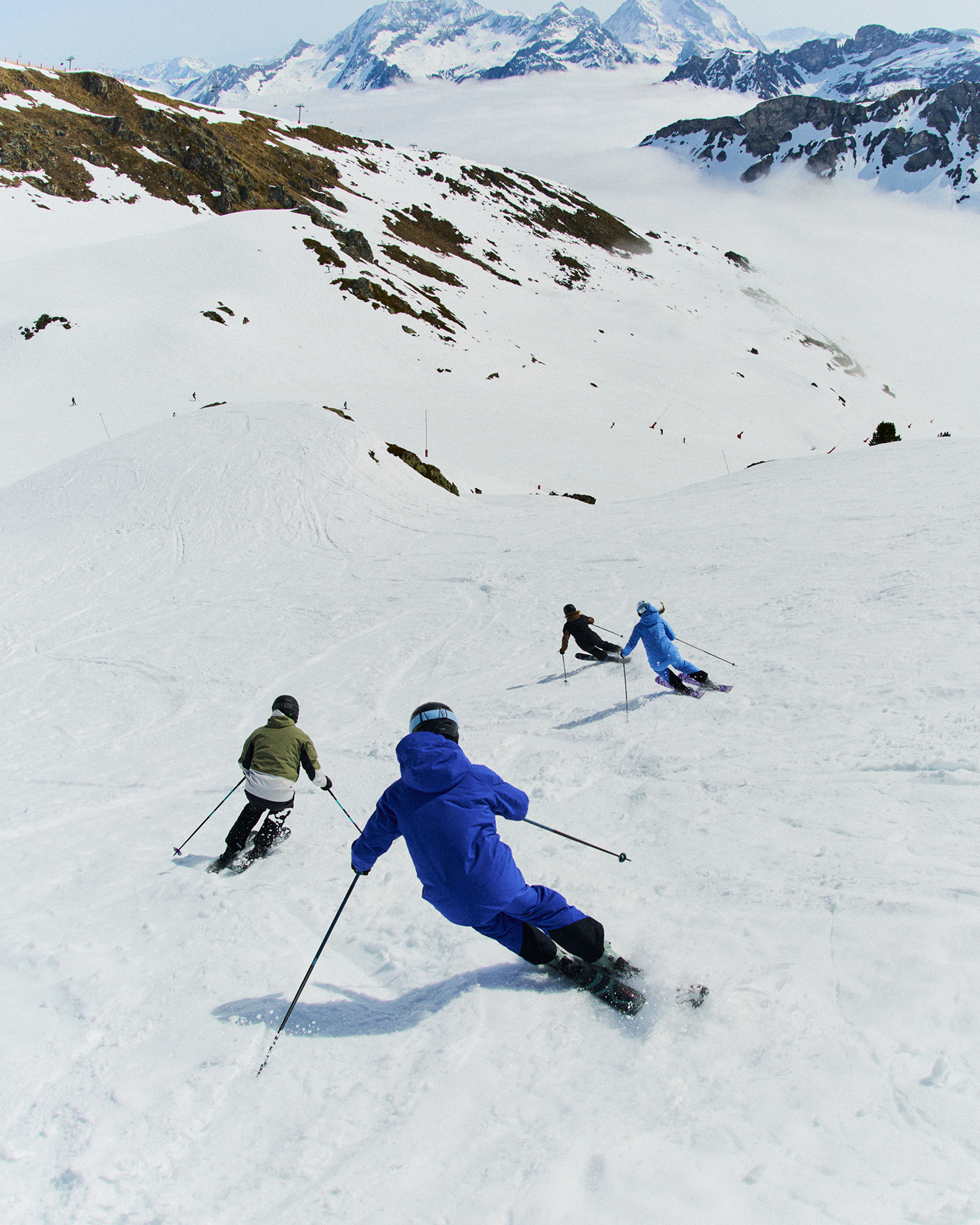 Four skiers gracefully descend a snowy mountain slope under a clear sky, showcasing skill and enthusiasm amidst stunning alpine scenery.