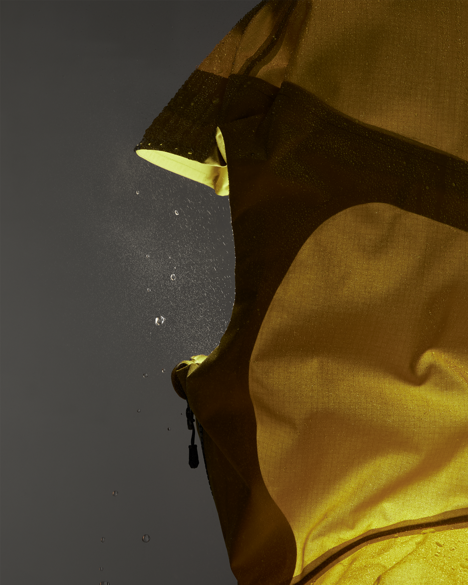 Close-up of a yellow raincoat with water droplets on the surface, highlighting the texture and waterproof material against a dark background.