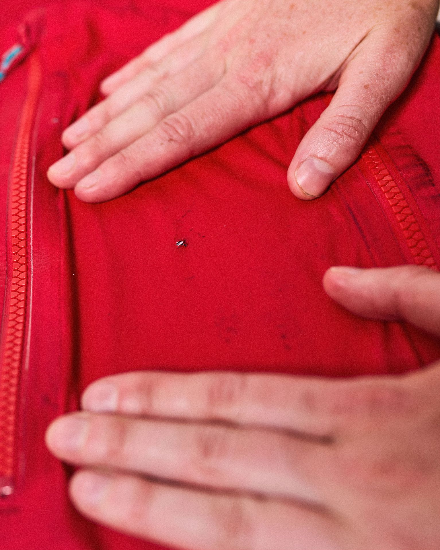 Hands showing a small hole in a red fabric jacket near a zipper.