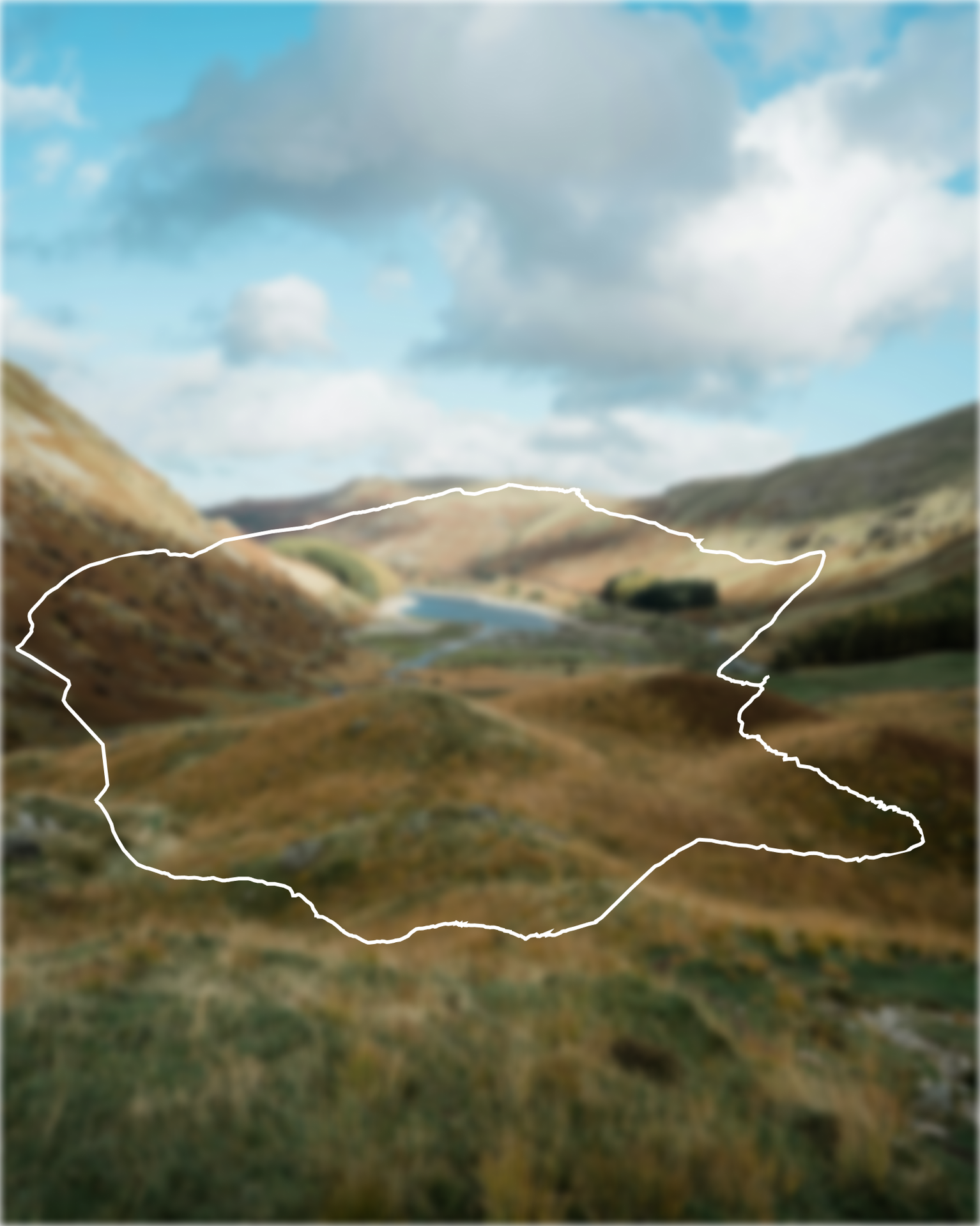 A scenic view of a valley with rolling hills, a winding path, and a distant lake under a partly cloudy sky.
