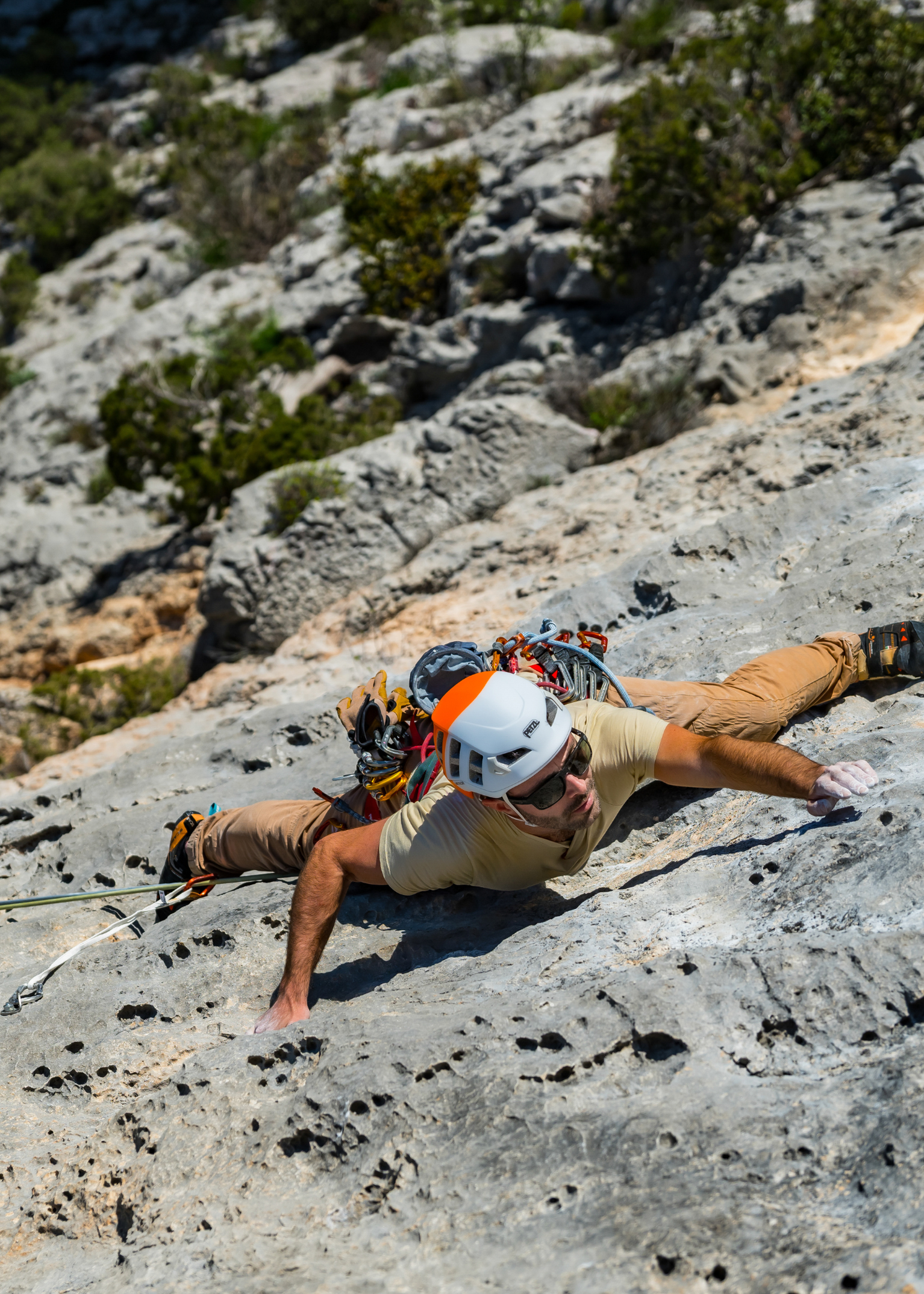 Person rock climbing on a rugged cliff face, wearing a helmet and harness, surrounded by greenery.