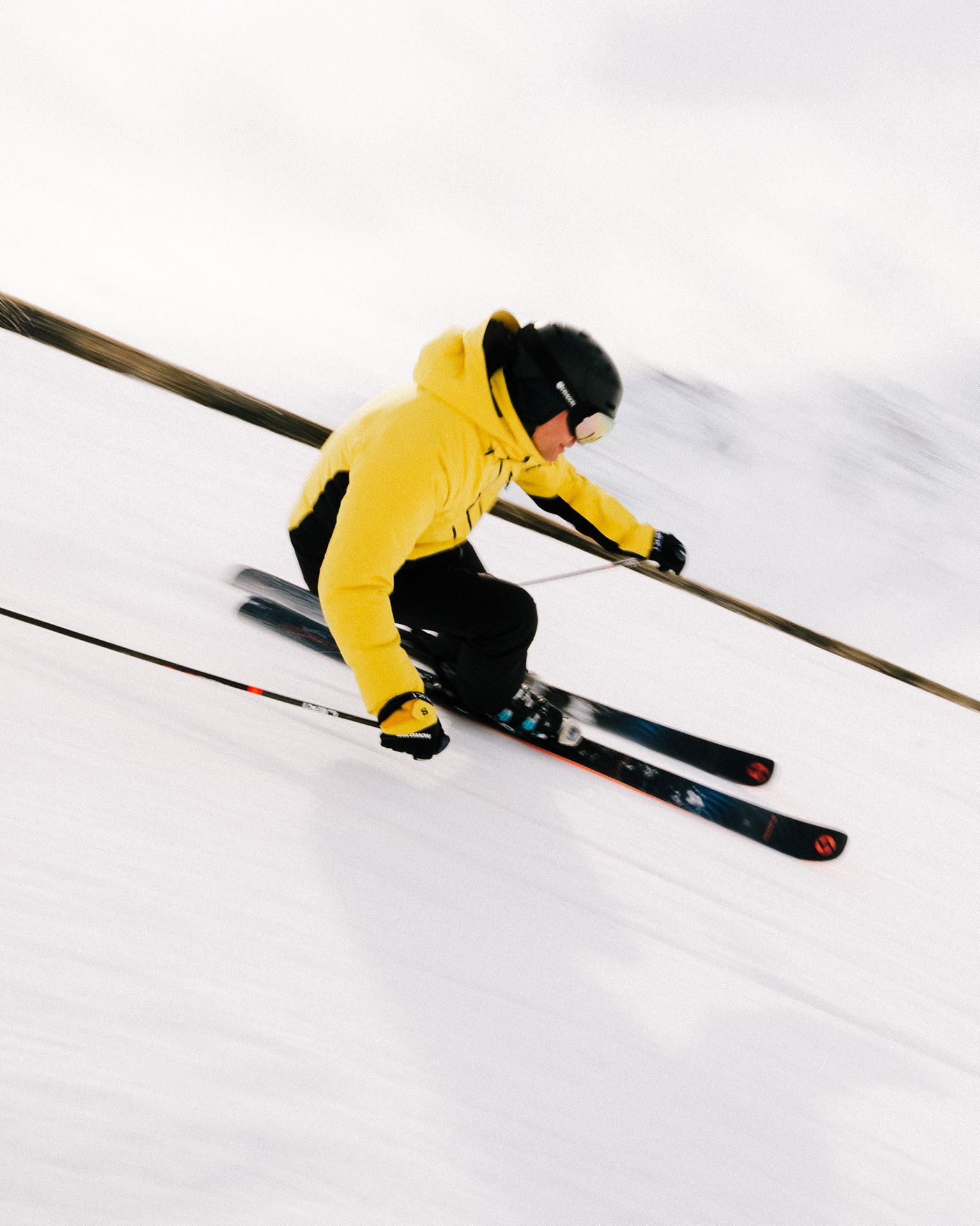 A skier in a yellow jacket and black helmet swiftly descends a snowy slope, showcasing dynamic motion and skill.