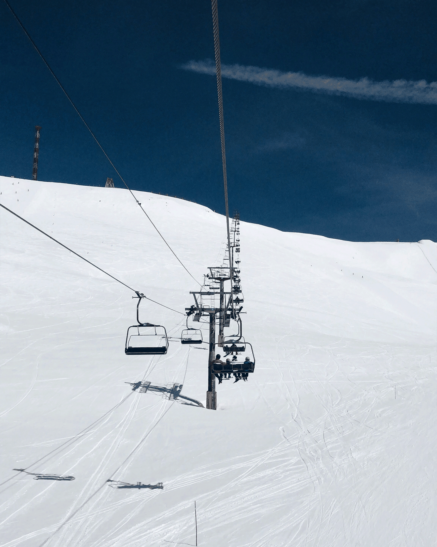 Ski chairlift ascending a snowy mountain under a clear blue sky.