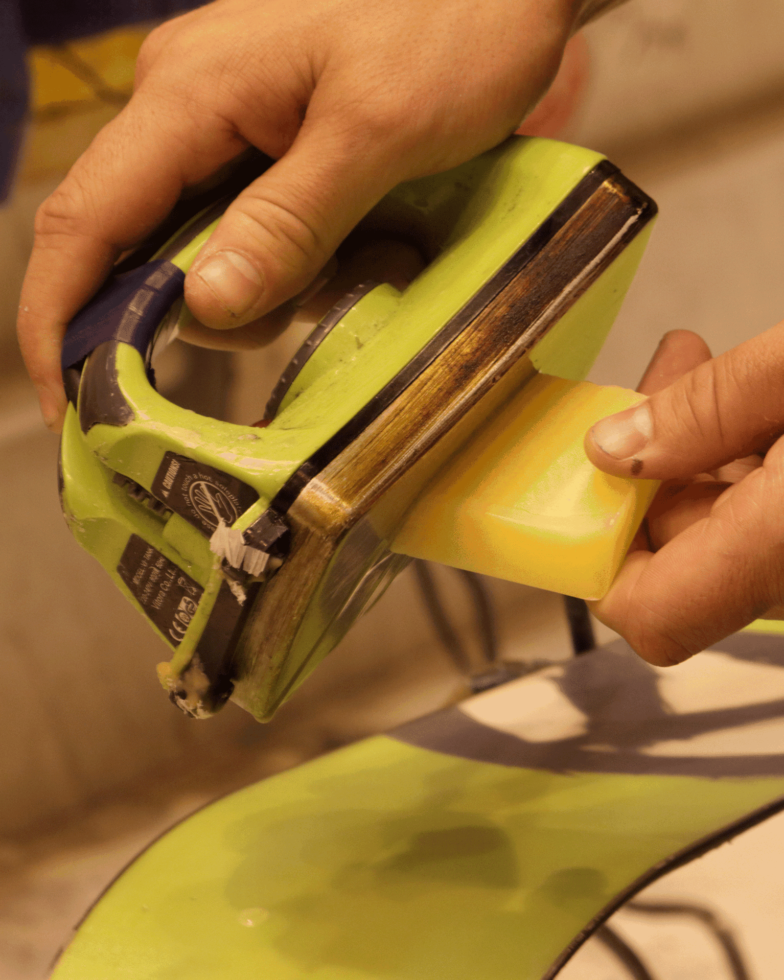 Hands holding an iron while waxing a ski with a yellow wax block.