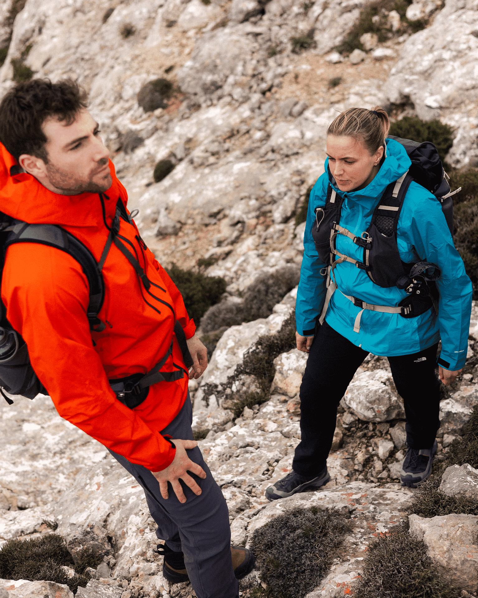 Two hikers in vibrant jackets navigate a rocky terrain, showcasing durable outdoor gear designed for challenging mountain adventures.