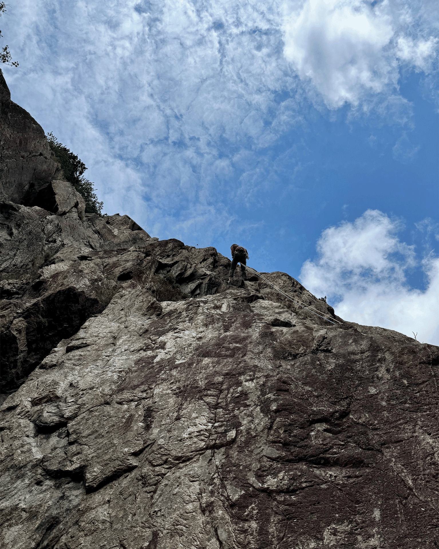 Rock climber ascending a rugged cliff under a vibrant blue sky with scattered clouds.