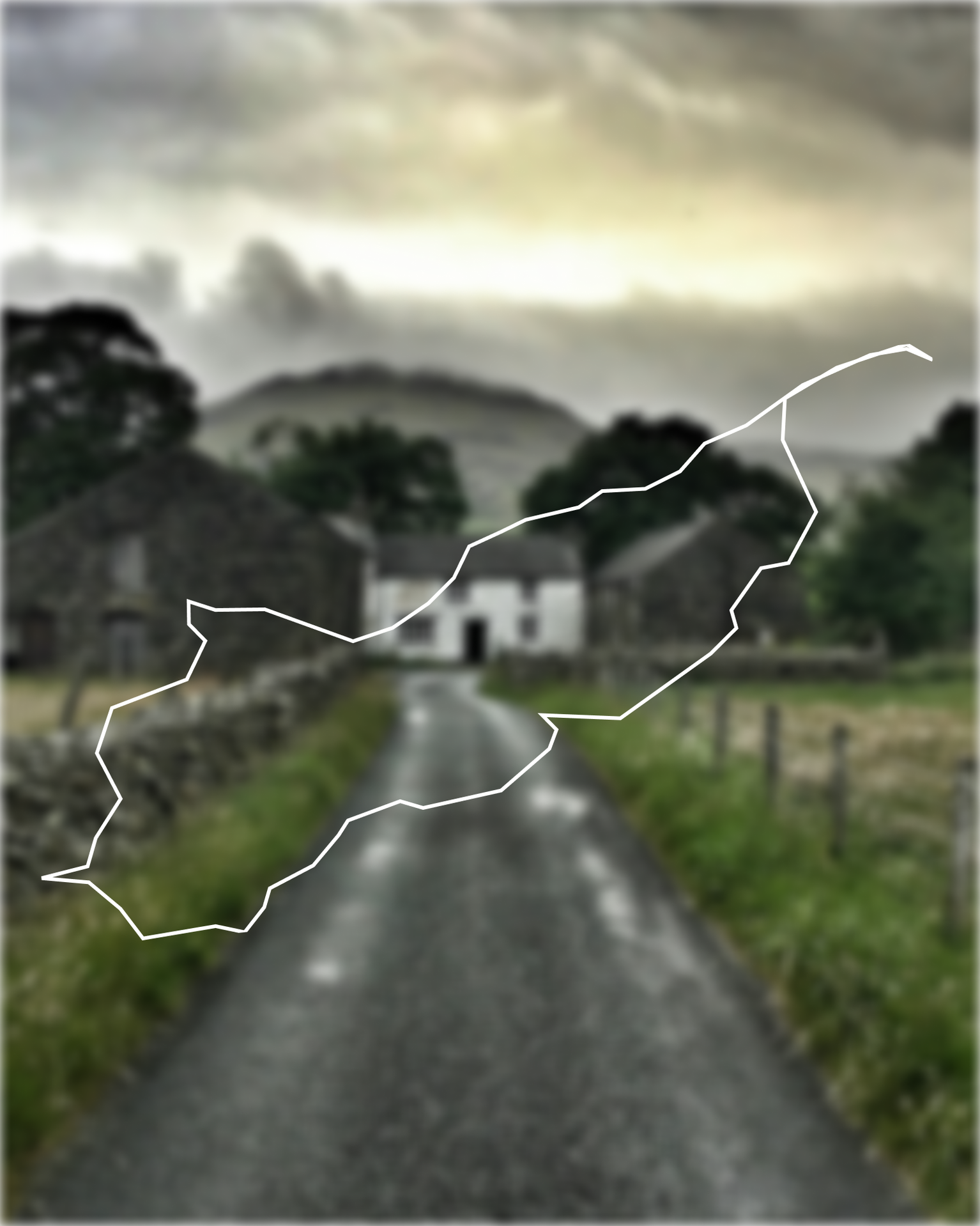 A narrow country road leads to a white house between stone buildings, with overcast skies and distant hills in the background.