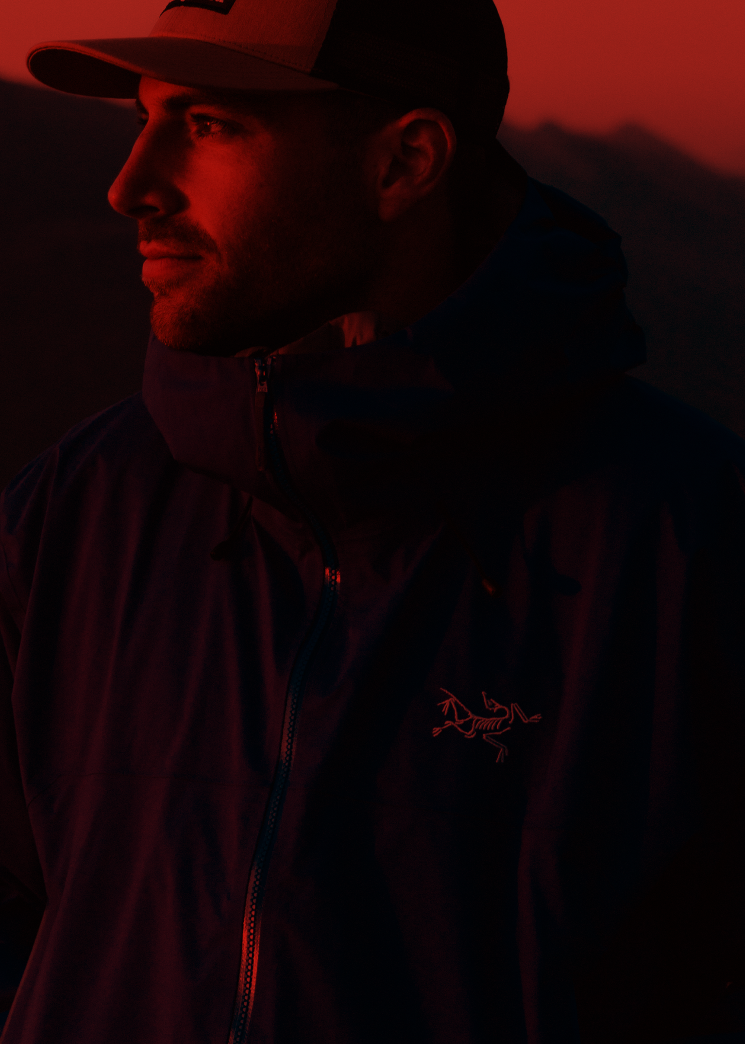 Man in an Arc'teryx jacket and cap, with mountains in the background.