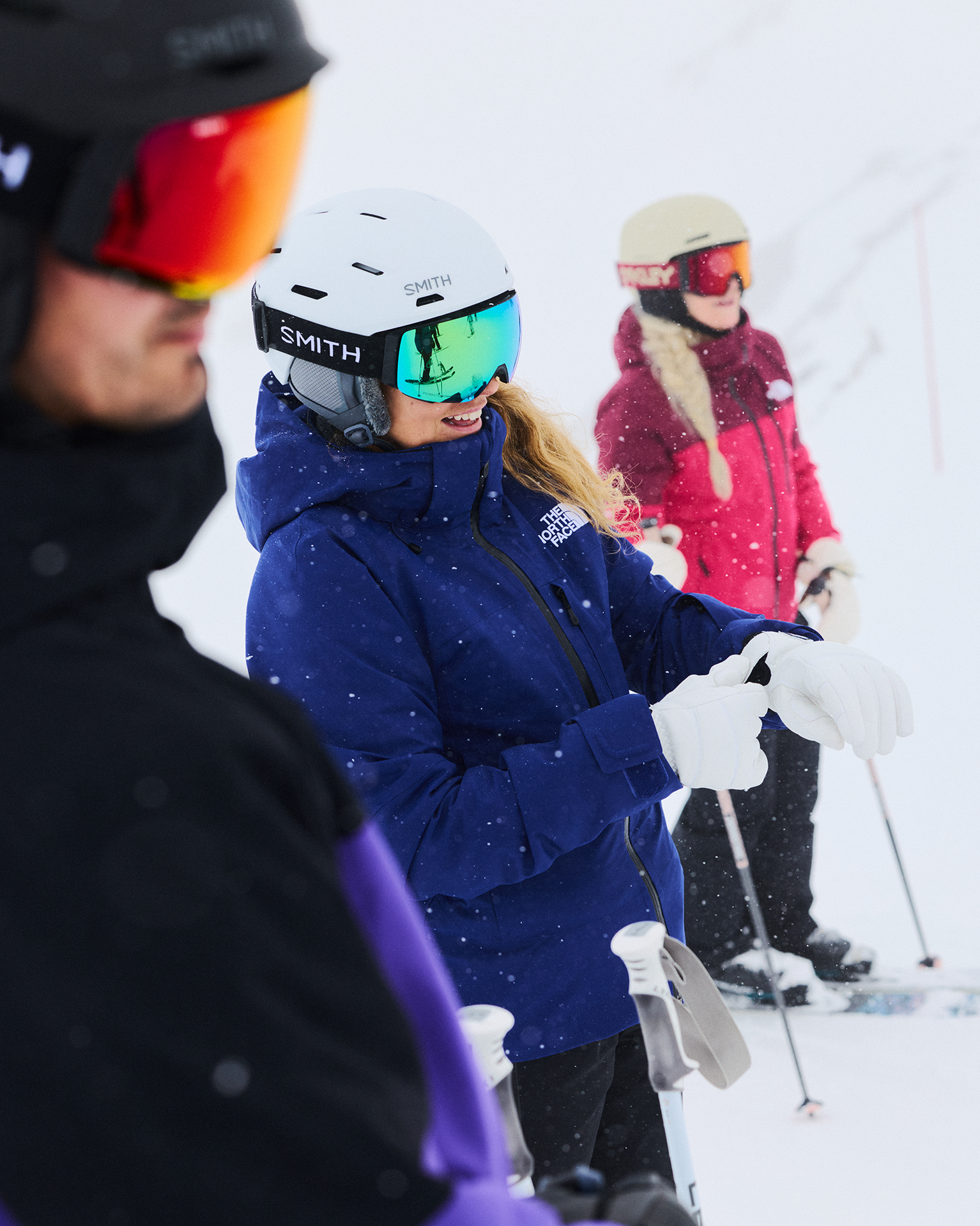 Three skiers in winter gear standing on a snowy slope, discussing their route.