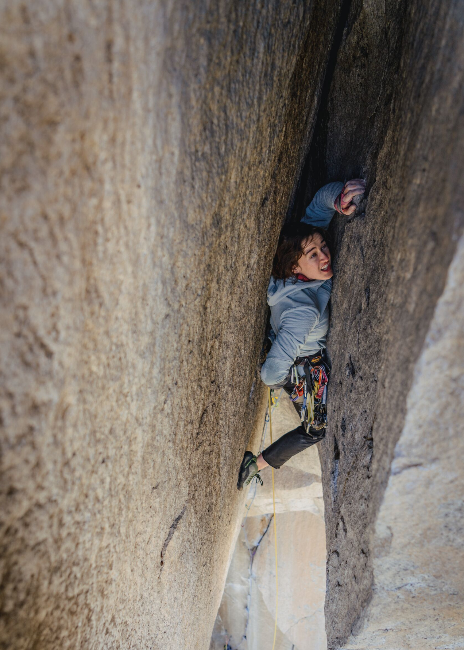 Climber navigating a narrow rock crevice, wearing a grey jacket and climbing gear, focused on ascent.