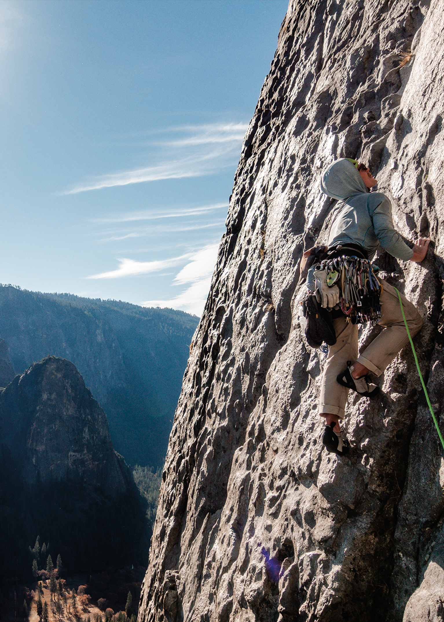 Climber scaling a rugged mountain face, wearing climbing gear. Scenic view of distant mountains under a clear blue sky.