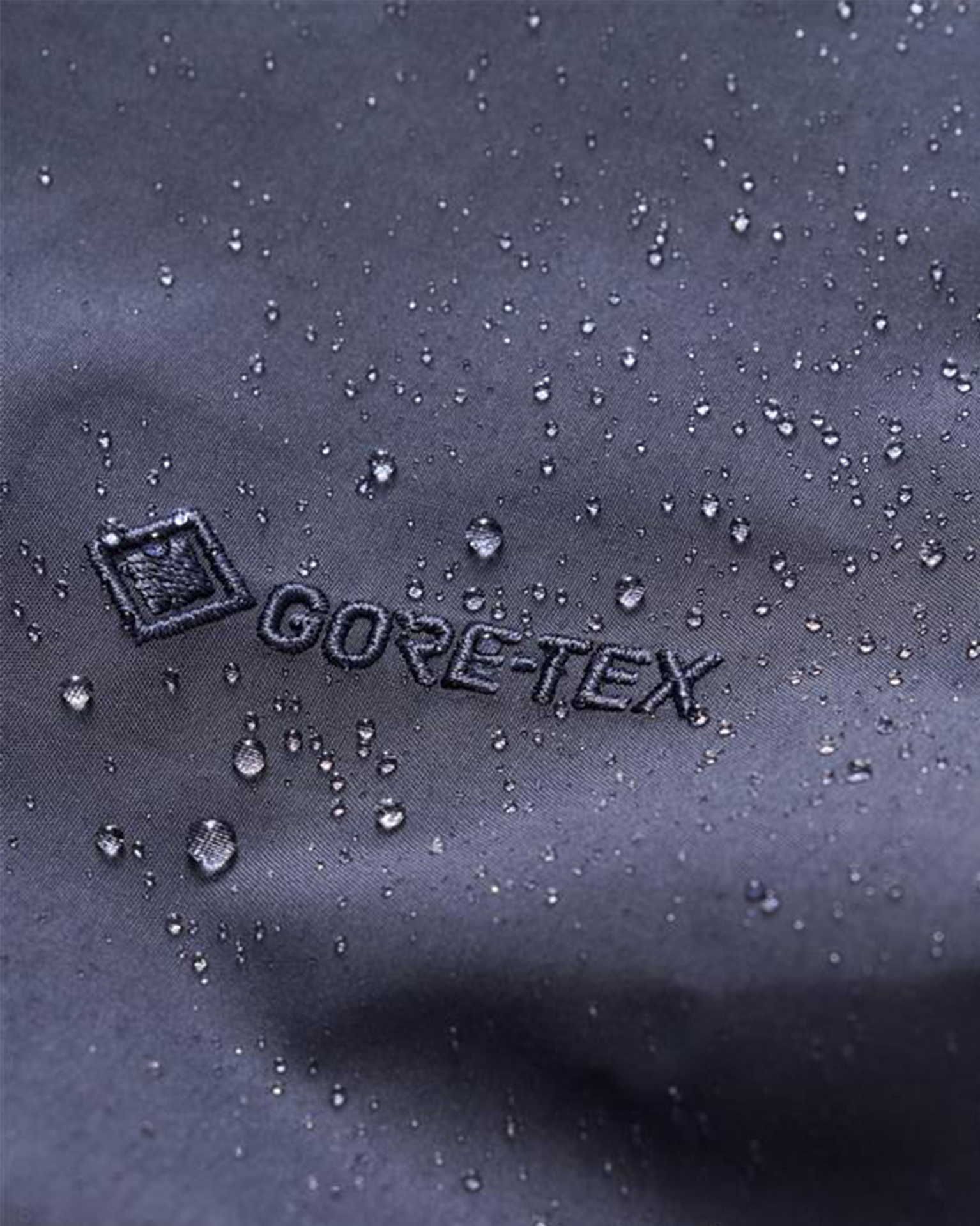 Close-up of a dark Gore-Tex fabric with water droplets beading on the surface, showcasing its water-resistant properties.