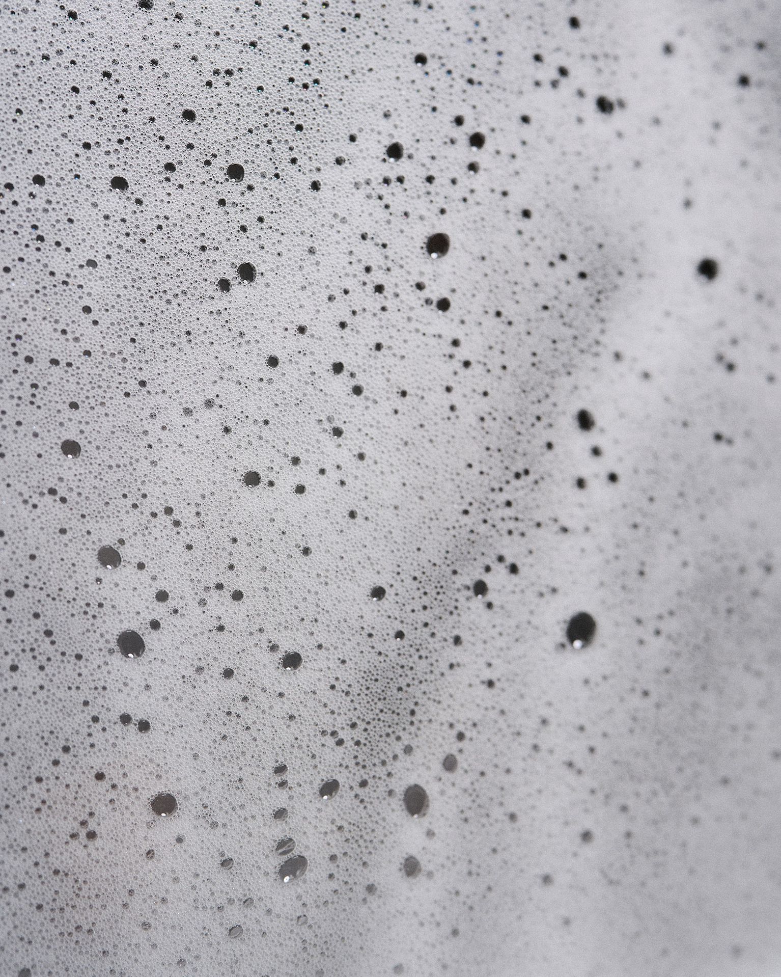 Close-up of white soap suds with various-sized bubbles spread across the surface, creating a textured and foamy appearance.