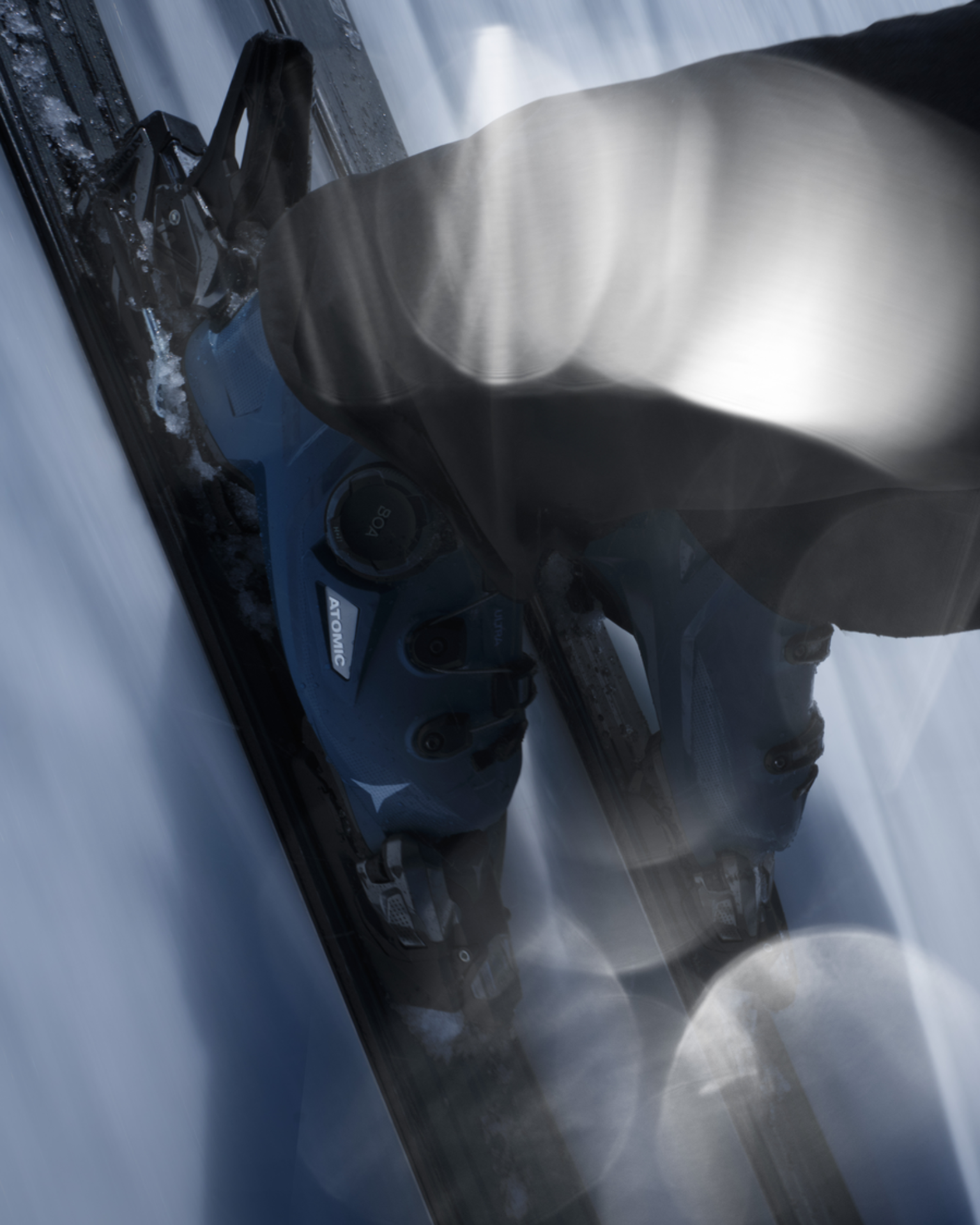 Close-up of a skier's blue ski boots and bindings on skis, gliding swiftly over snow with motion blur and light reflections.