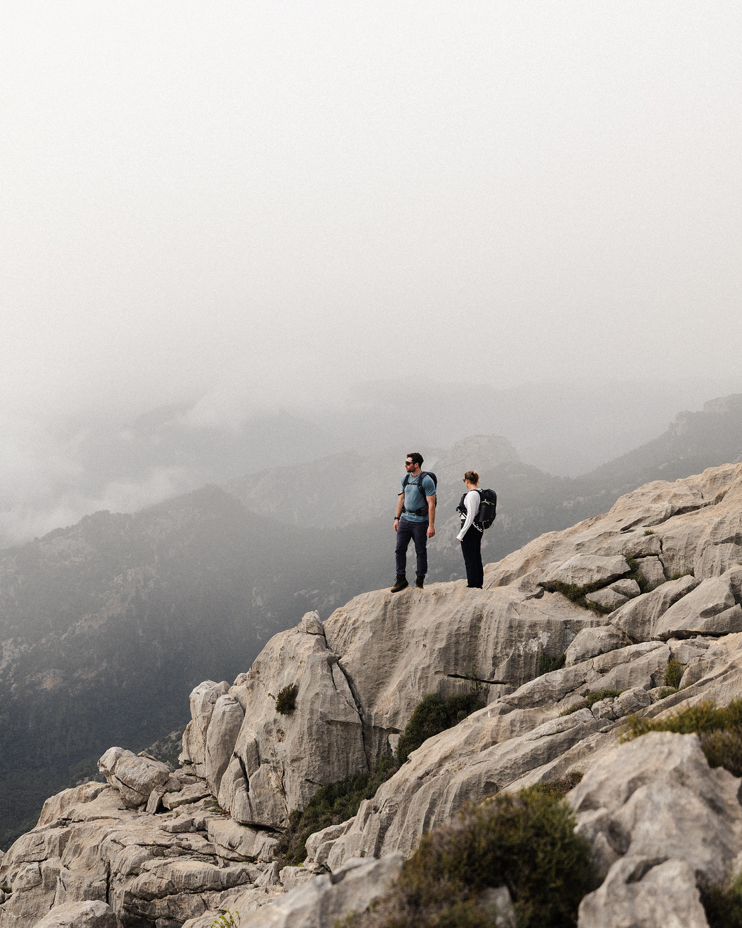 Two hikers standing on a rocky mountain edge, overlooking a misty valley below.