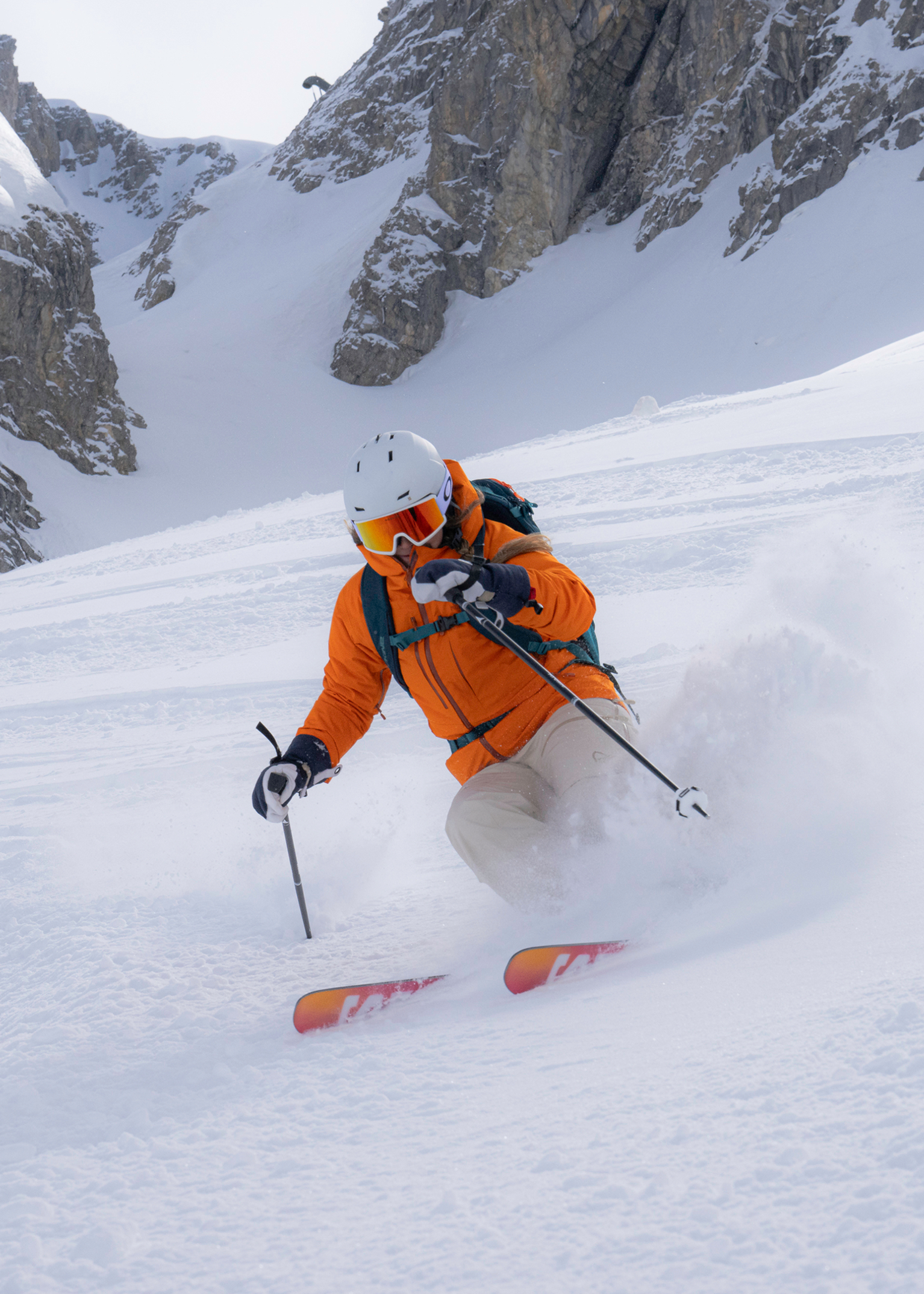 A skiier in an orange ski jacket skis down