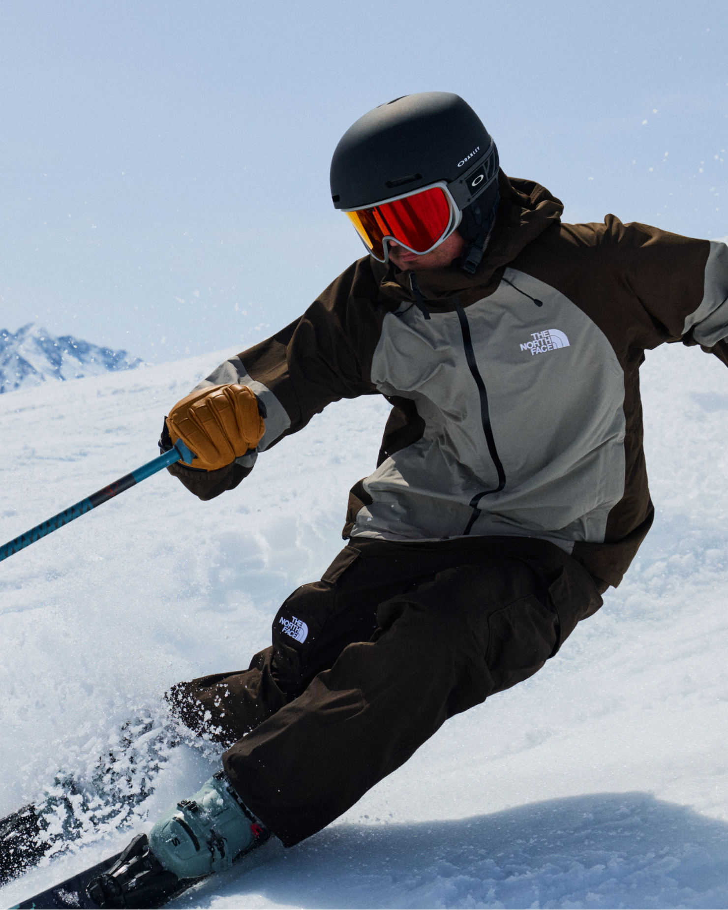 A skier confidently carves through snow wearing high-quality mountain sports gear, including a helmet and goggles, under a clear blue sky.