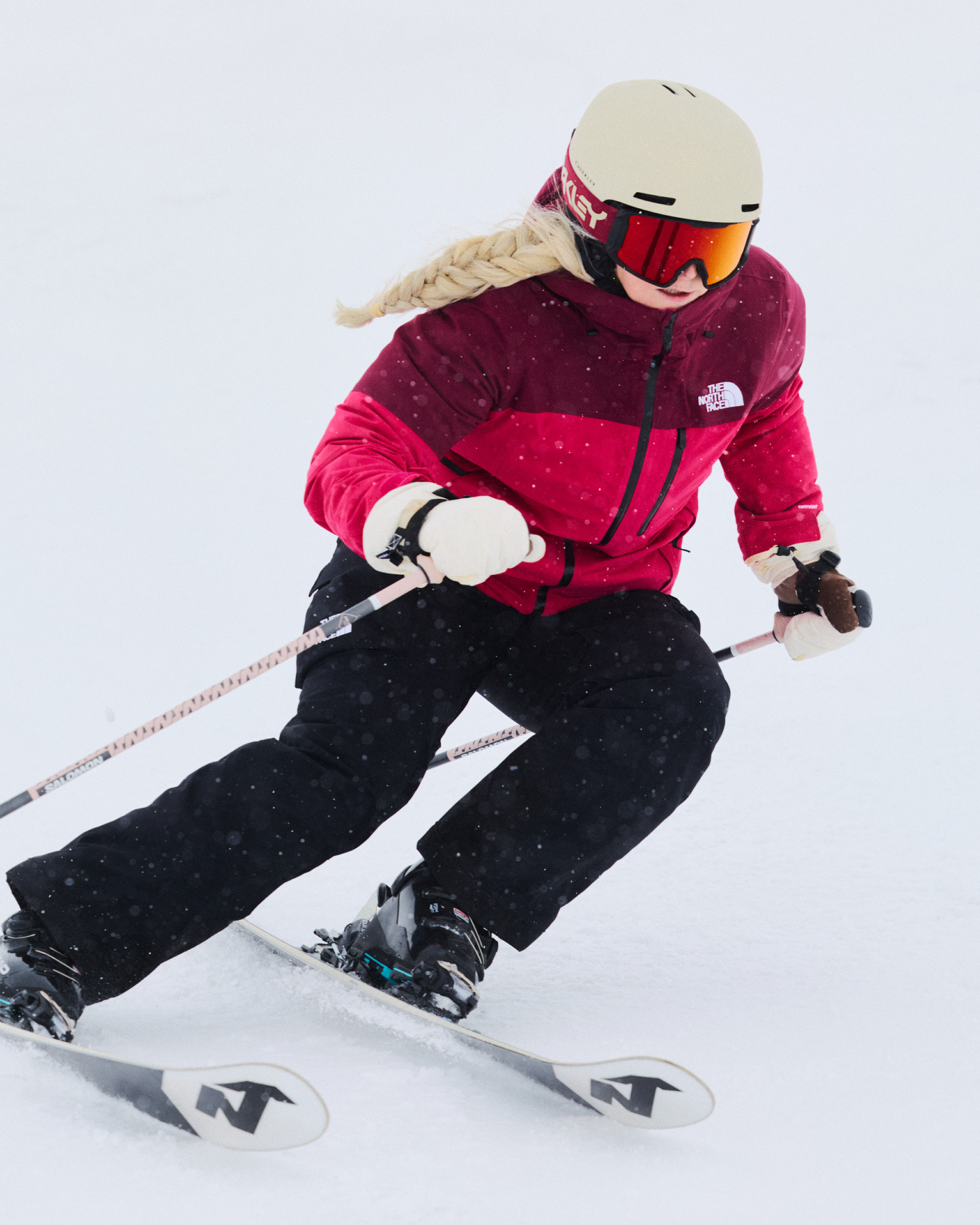 A skier in a red ski jacket and black pants expertly carves through the snow, showcasing dynamic movement on the slopes.