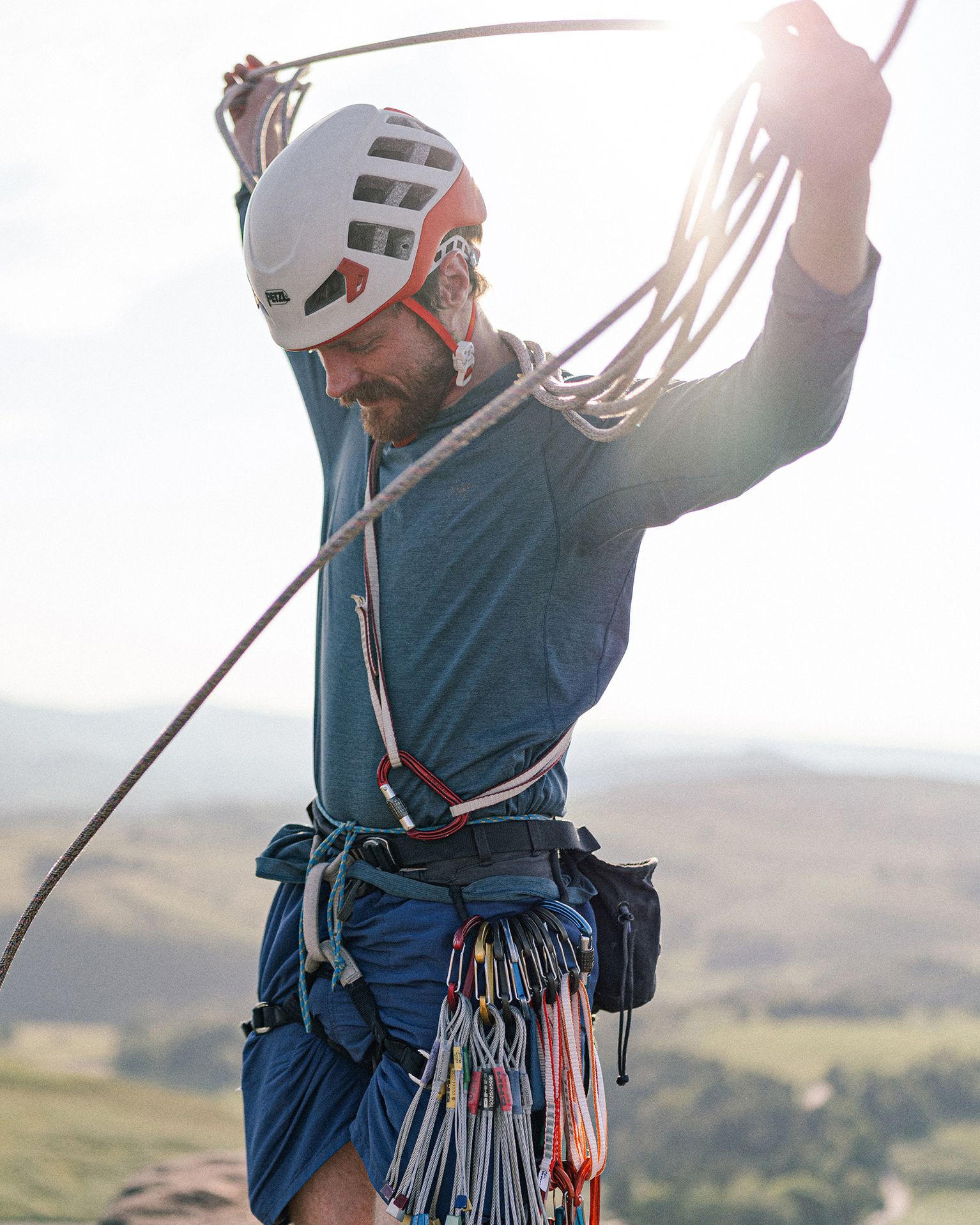 Man in climbing gear holding rope, standing on a rock under a clear sky.