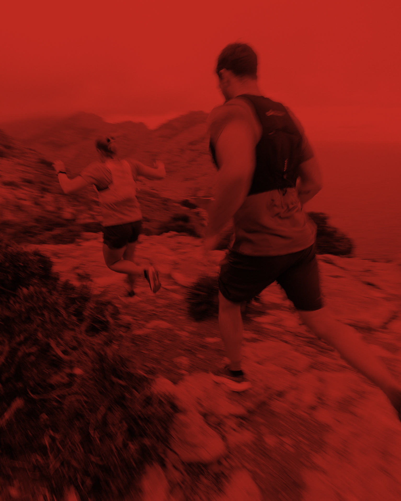 Two runners on a rocky mountain trail, captured in motion with a dramatic red filter.