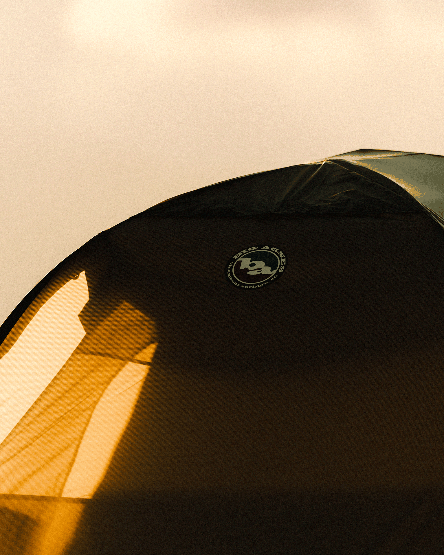 Close-up of a tent with sunlight casting shadows on its fabric, featuring a logo.