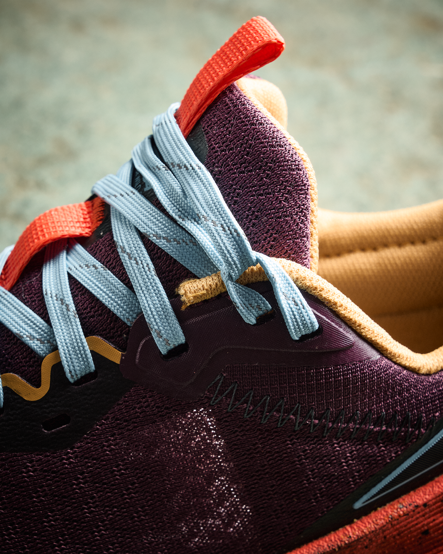 Close-up of a colourful trainer with purple mesh, light blue laces, and red accents, showcasing intricate stitching and textured fabric.