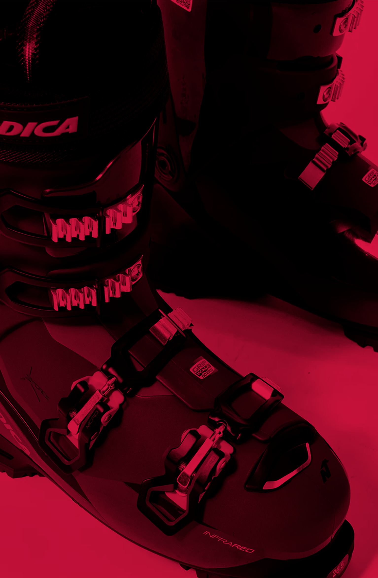 Close-up of black ski boots with red accents and multiple buckles, placed on a red-tinted surface.